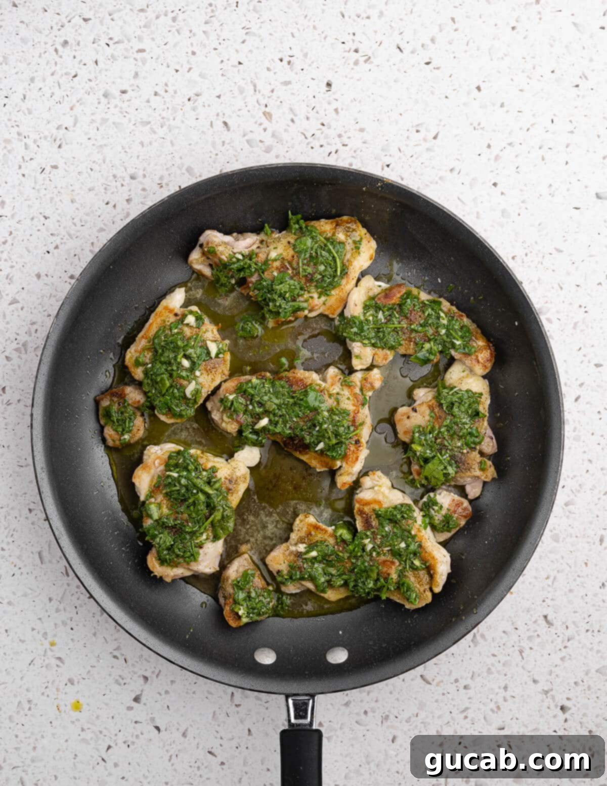 Zesty Chimichurri Chicken Thighs 10 Caramelized chicken thighs in a skillet, now generously covered with fresh chimichurri sauce, ready for the oven.