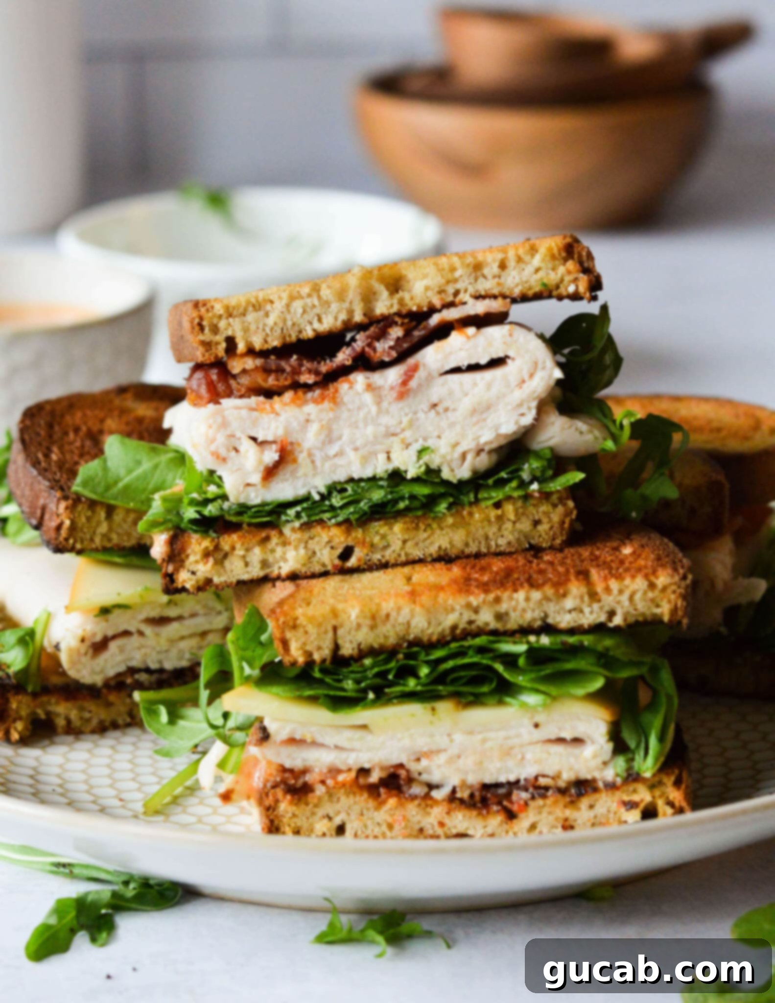 A gourmet turkey sandwich, showcasing the layers of fresh ingredients like arugula, bacon, and thinly sliced turkey, served on toasted sourdough.