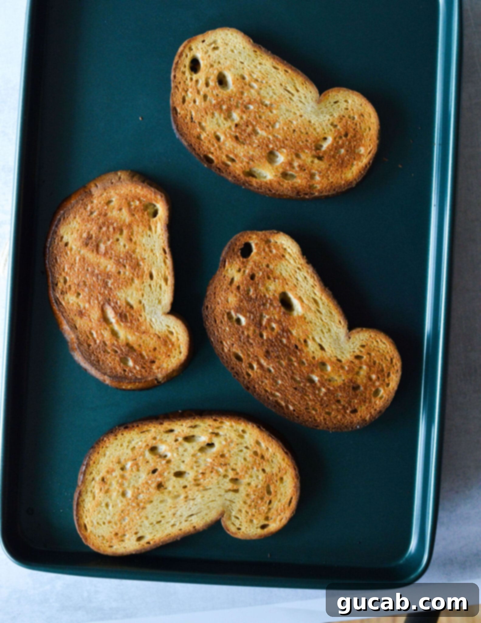 Golden-brown toasted sourdough bread slices resting on a sheet pan after broiling, showing their crisp texture.