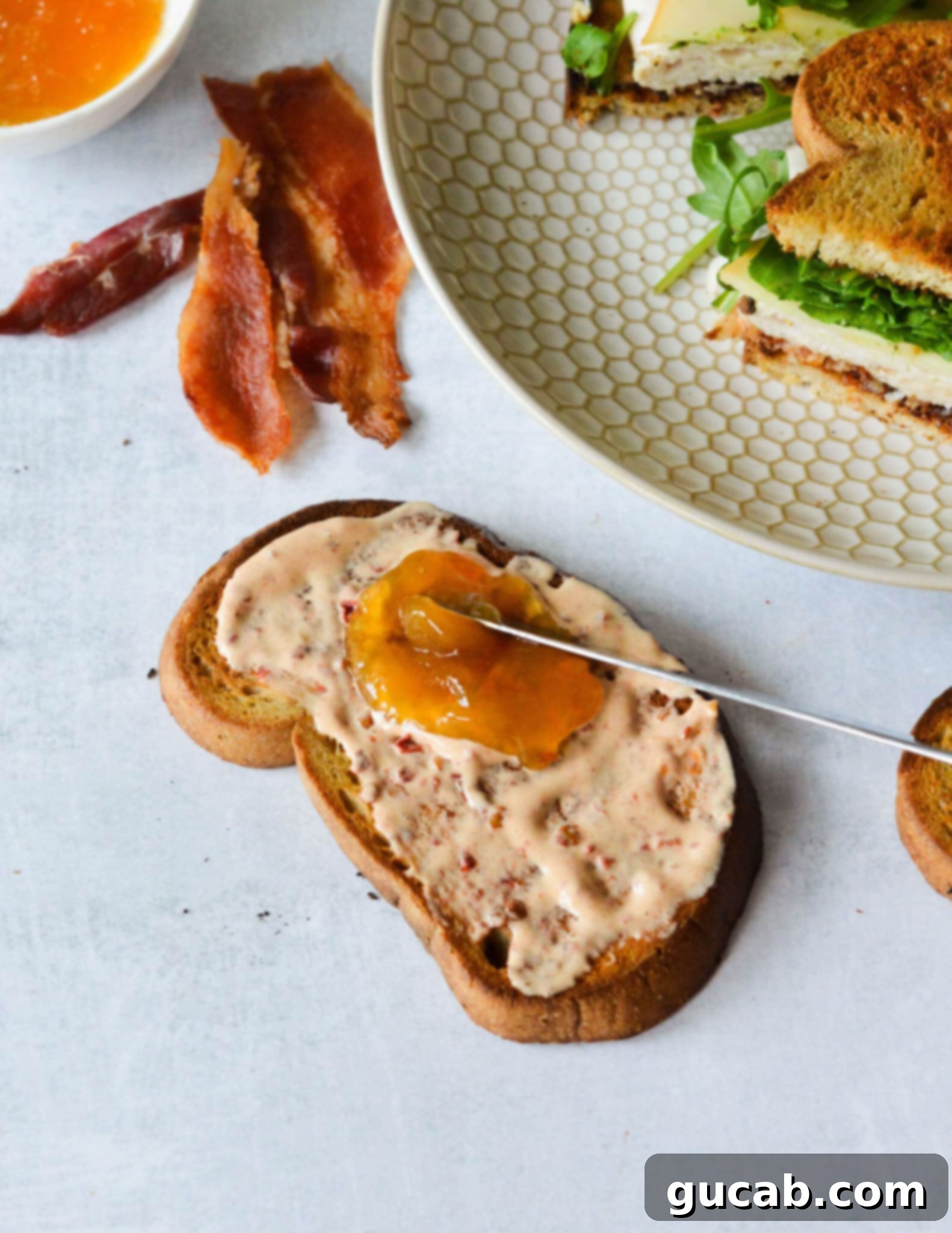 Spreading sweet apricot jam on a slice of toasted sourdough bread, which already has a layer of chipotle mayo.
