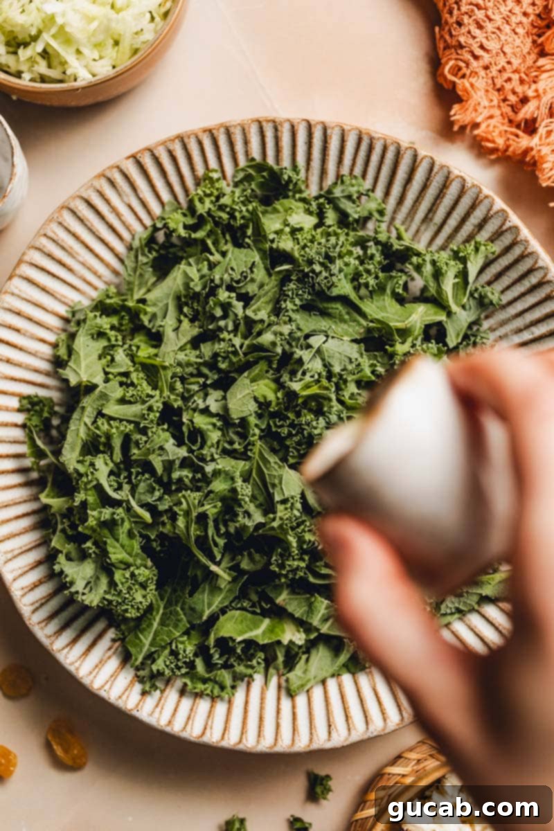 A hand pouring a small amount of olive oil onto a bowl filled with fresh, green kale leaves.