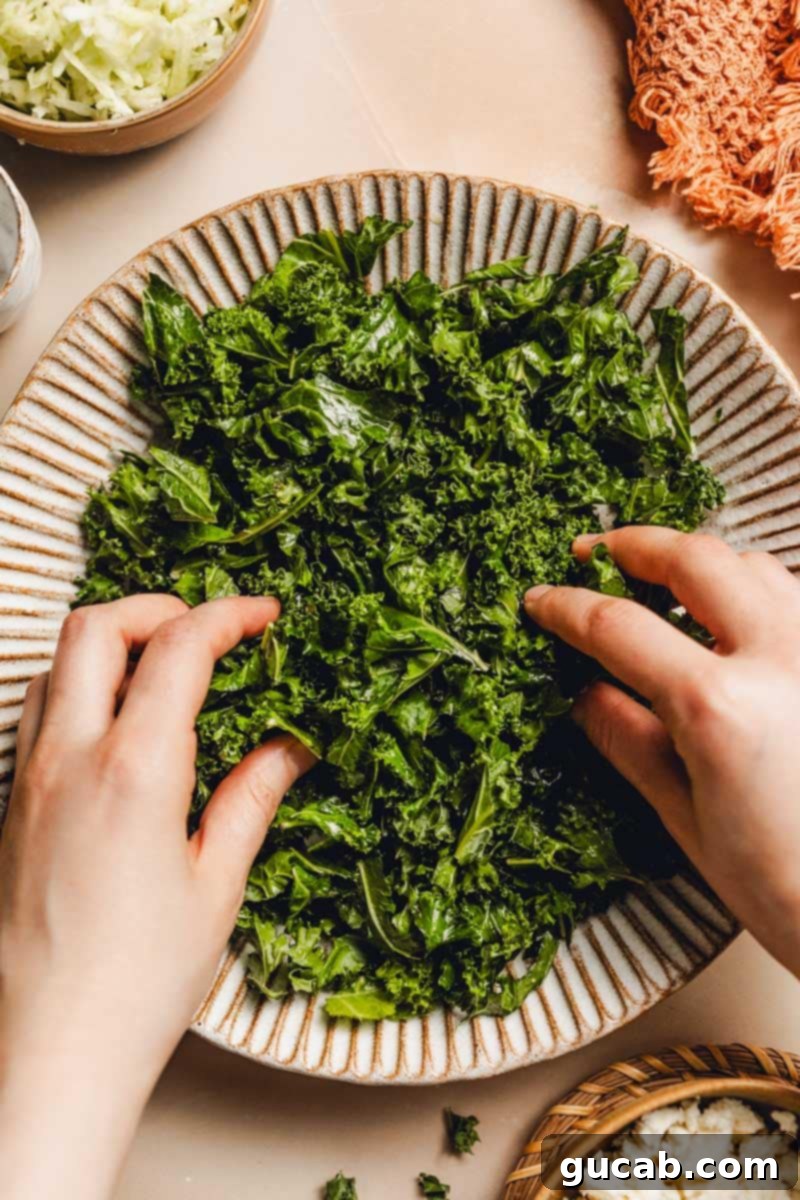 A hand gently massaging olive oil into the kale leaves in a bowl, softening them for the salad.