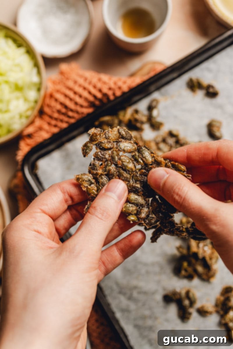 Hands gently breaking apart the cooled, hardened maple pepitas into smaller, manageable pieces.