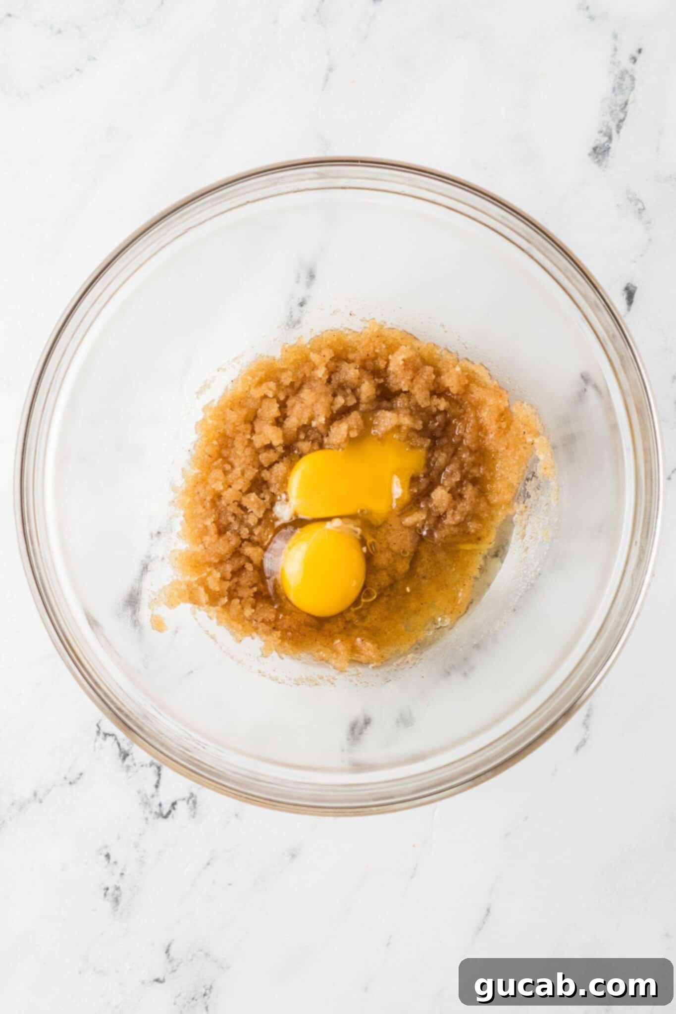A bowl of the sugar, brown sugar, and butter mixture with a whole egg and an egg yolk resting on top, ready to be incorporated.