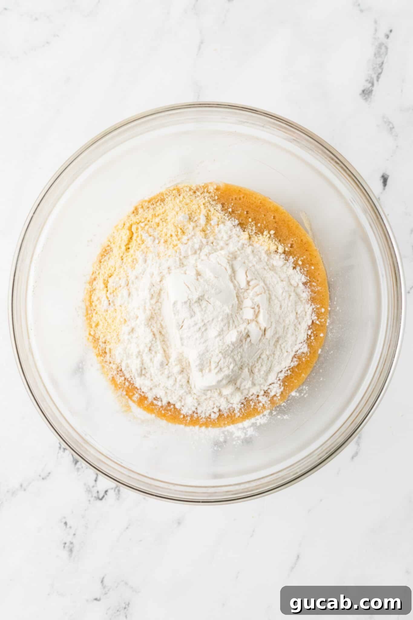 A bowl showing the wet mixture with flour and yellow cornmeal added on top, ready to be folded into cookie dough.
