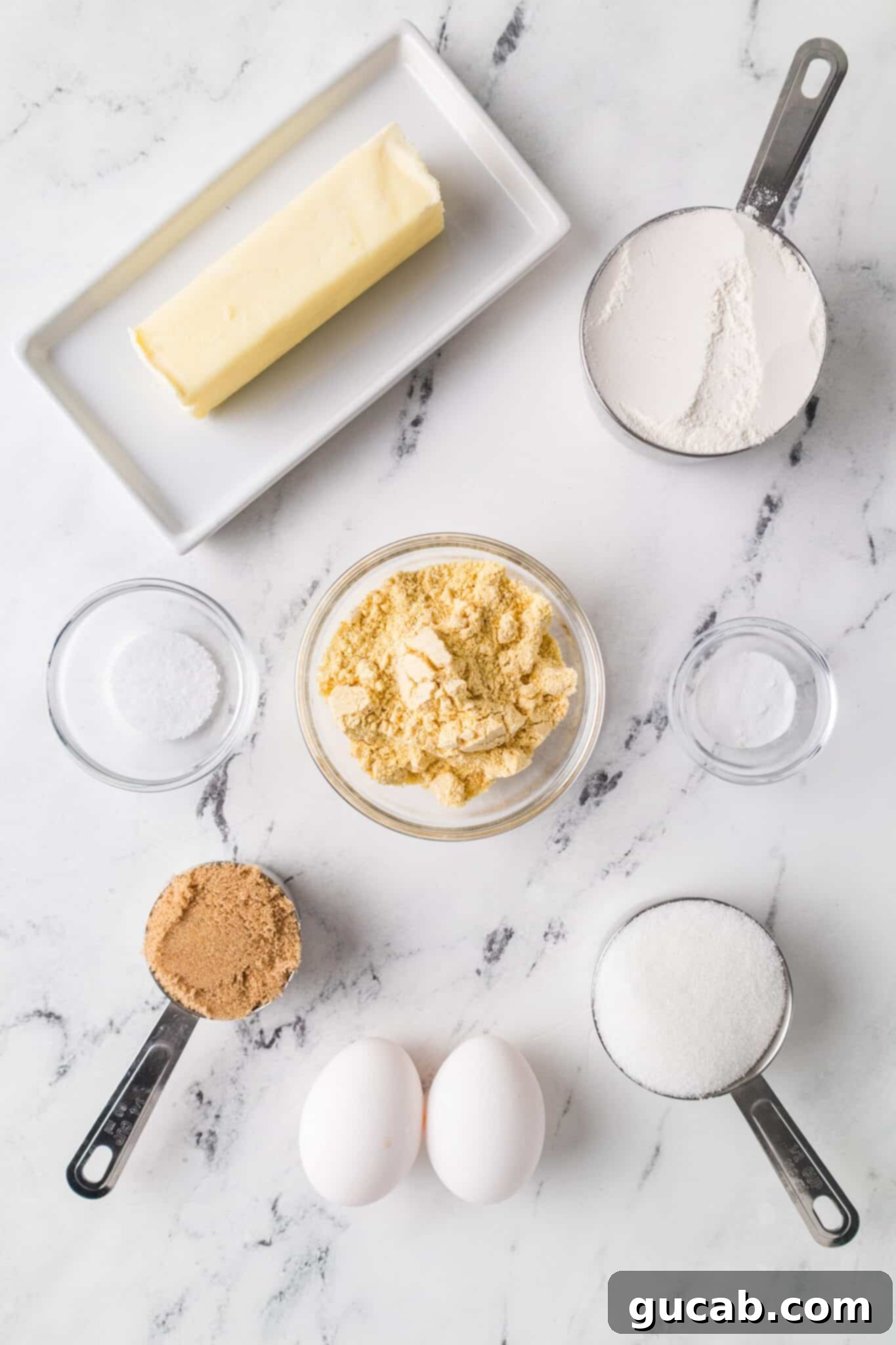 A flat lay photograph showcasing the key ingredients for cornmeal cookies: unsalted butter, granulated sugar, brown sugar, a large egg, an egg yolk, all-purpose flour, yellow cornmeal, baking soda, and kosher salt.