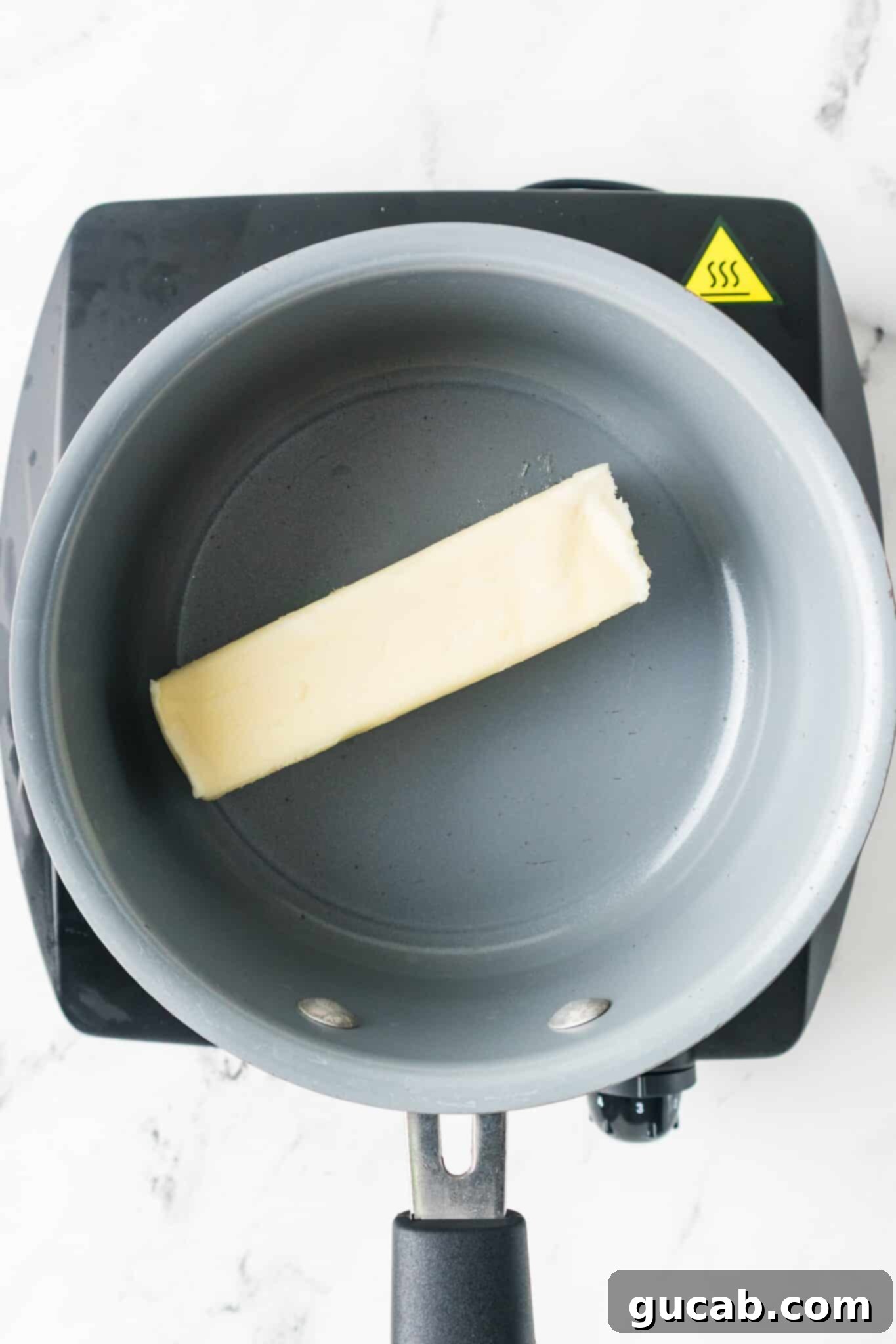 A pot on the stovetop with a stick of unsalted butter beginning to melt.