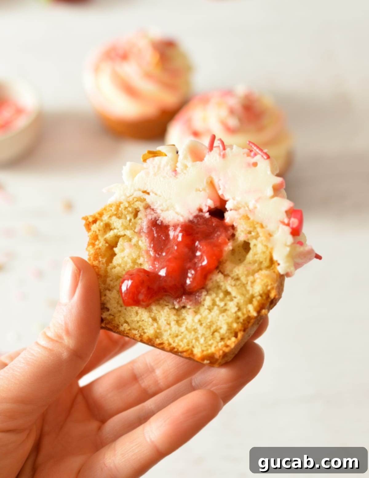 A hand holding a perfectly baked gluten free cupcake with strawberry filling, highlighting its texture.