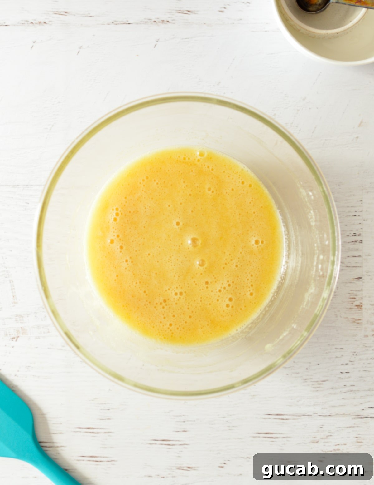 A bowl of fully beaten egg, sugar, and oil mixture, smooth and emulsified.