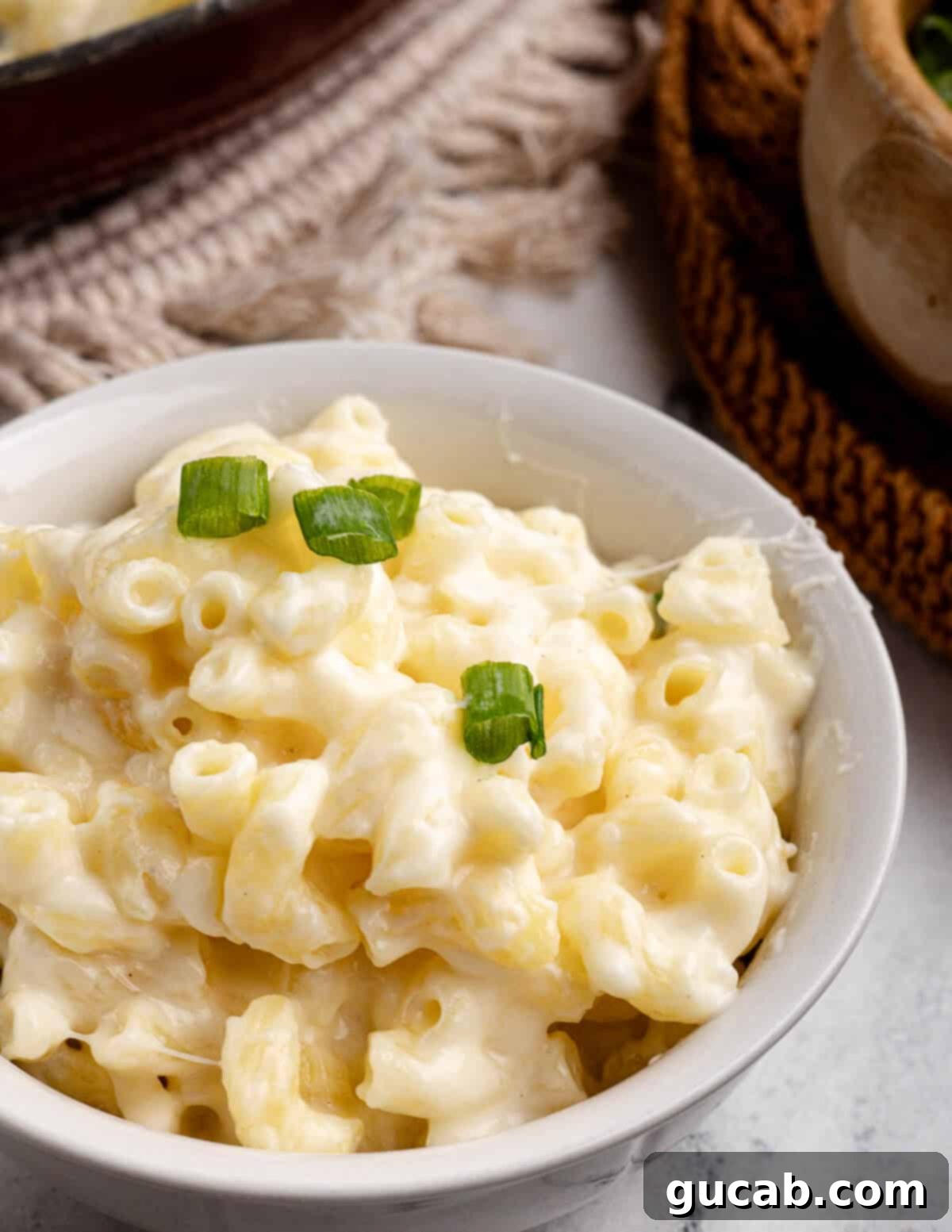 A steaming bowl of creamy gluten-free macaroni and cheese, garnished with fresh green onions.