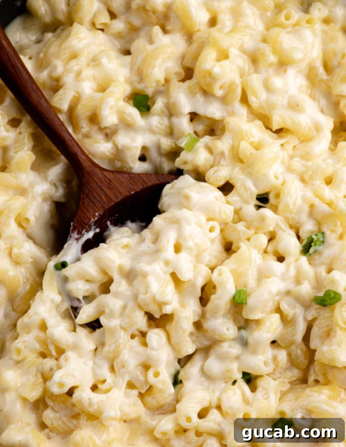 A large wooden serving spoon deeply embedded in a bowl of hot, gooey gluten-free macaroni and cheese, ready to be scooped.