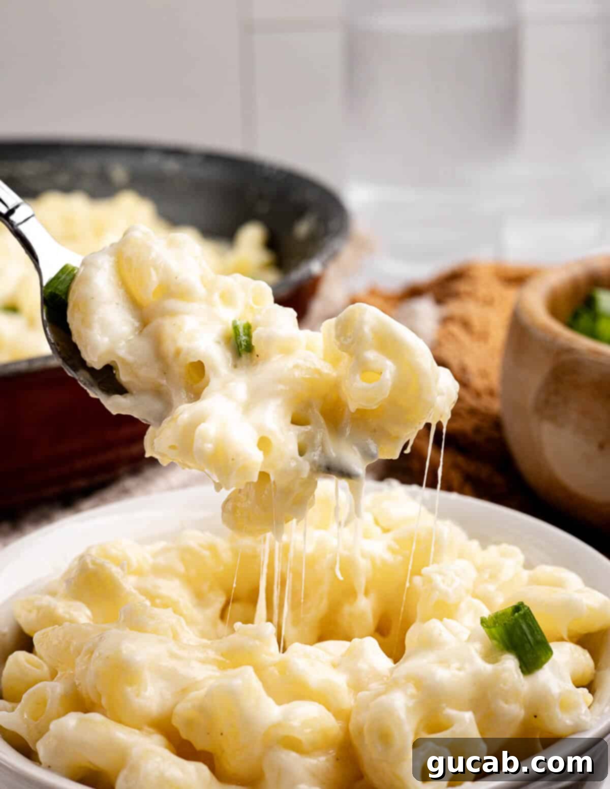 A close-up shot of a forkful of creamy gluten-free macaroni and cheese being lifted from a bowl, showing the rich, melted cheese and perfectly cooked pasta.