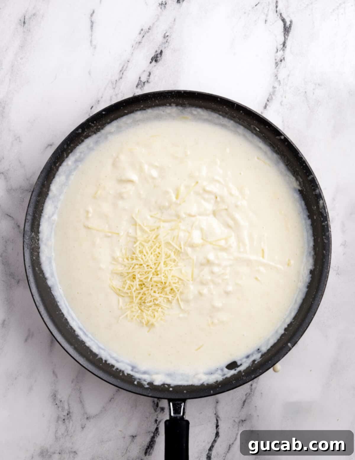 Rich, smooth cheese sauce forming in a skillet as the shredded cheese melts and blends.