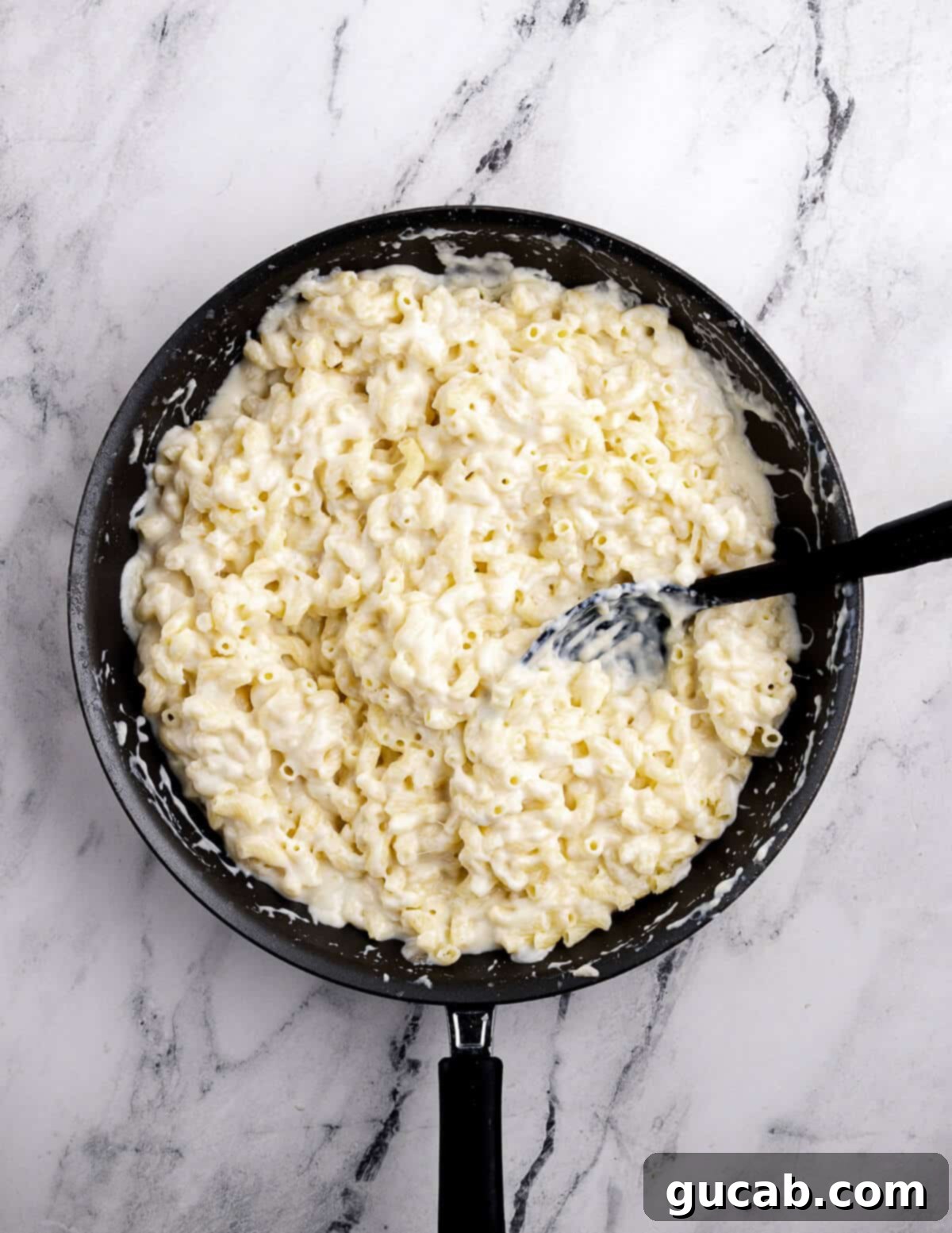 A skillet full of finished gluten-free macaroni and cheese, perfectly coated in rich, gooey cheese sauce.