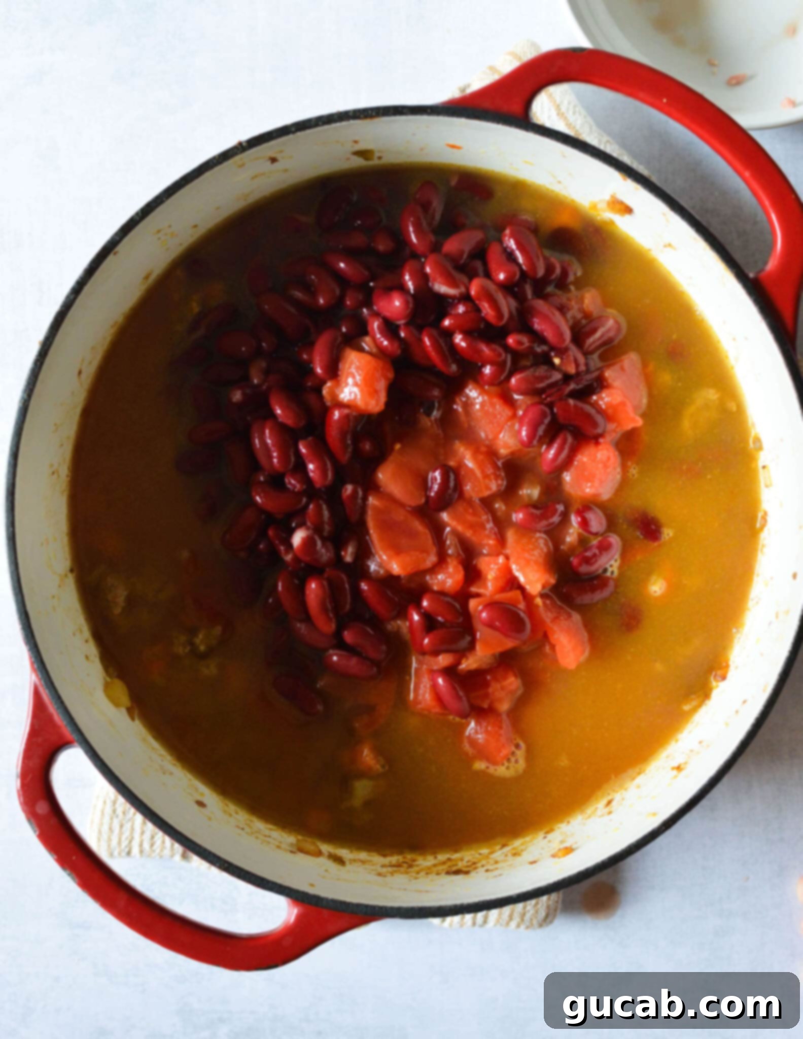 a pot with kidney beans and tomatoes in chicken stock in a pot. 