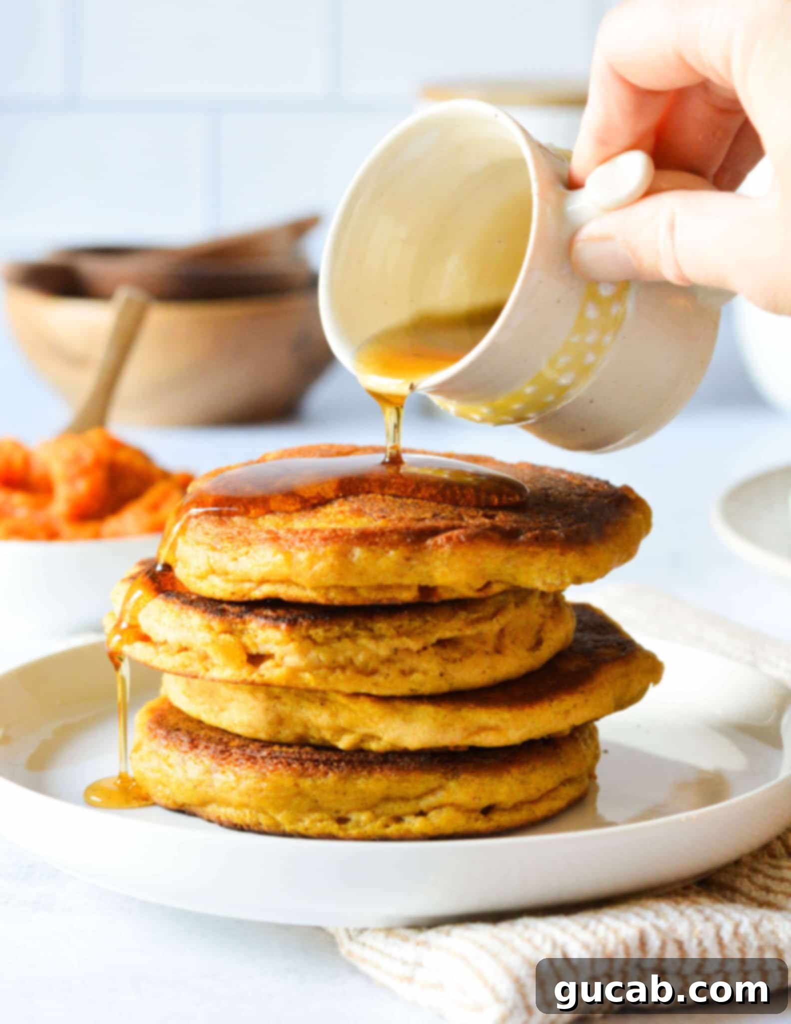 hand pouring maple syrup onto a stack of gluten free pumpkin pancakes.