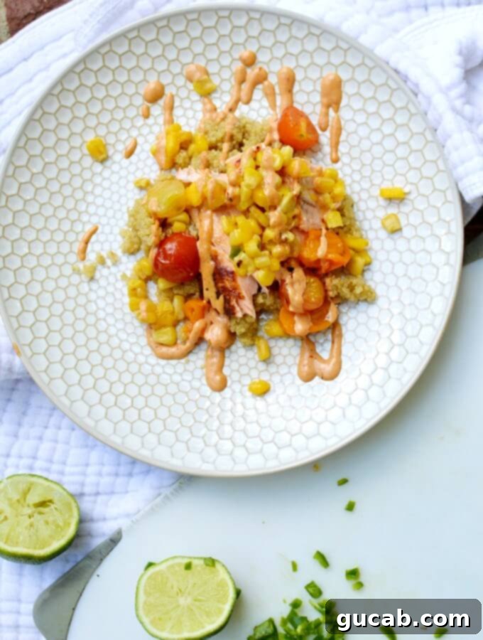 A vibrant salmon quinoa bowl with pan-seared salmon, fluffy quinoa, roasted tomatoes, corn, mango, jalapeno, and a drizzle of chipotle mayo.