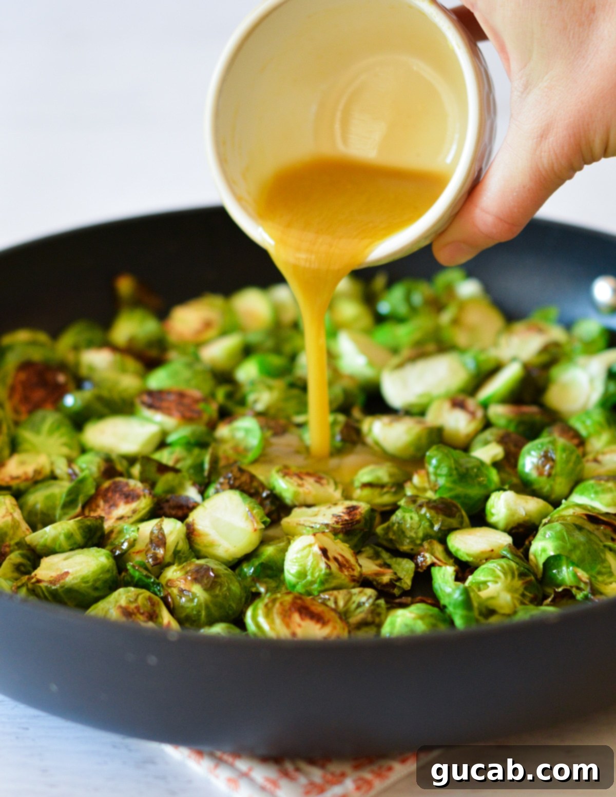 pouring maple sauce into brussels sprouts in a skillet. 