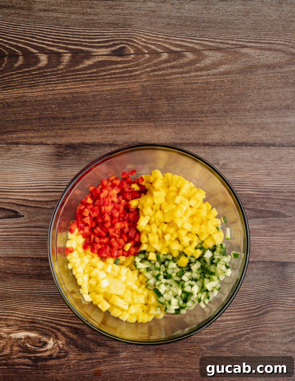 a bowl with diced mango, cucumber, pineapple, and red bell pepper in it. 