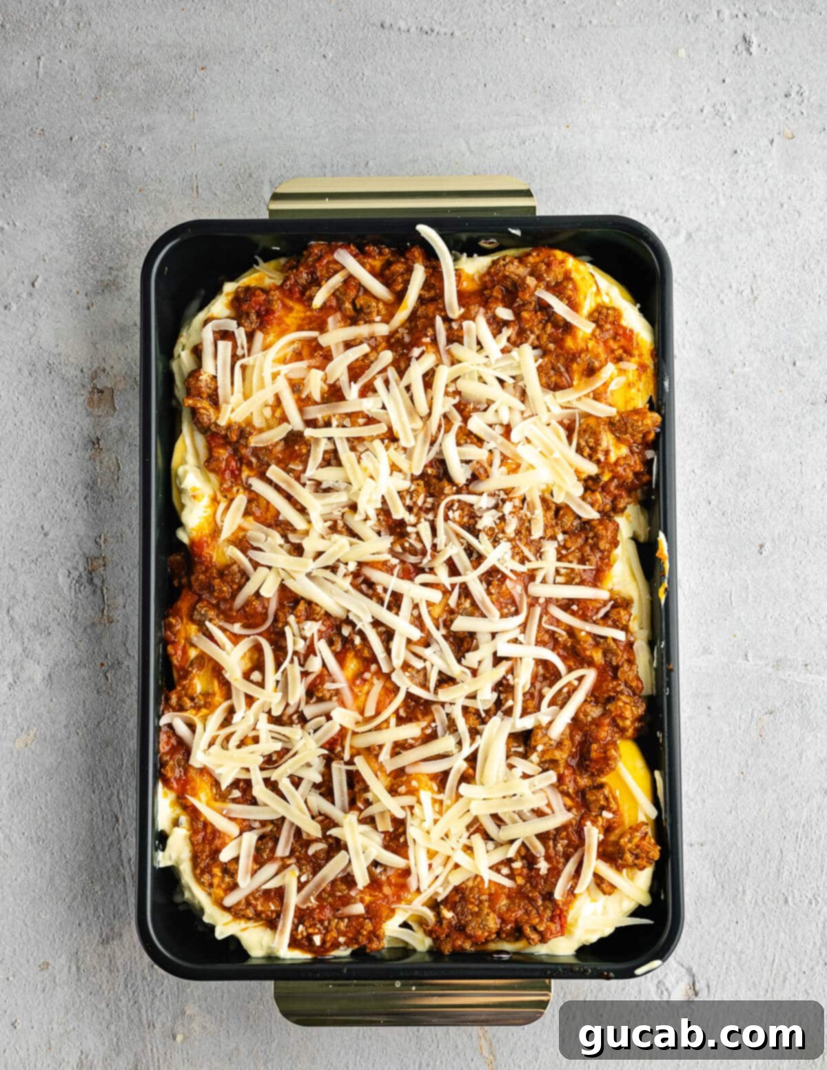 An unbaked butternut squash lasagna showing all layers topped with cheese, ready for the oven.