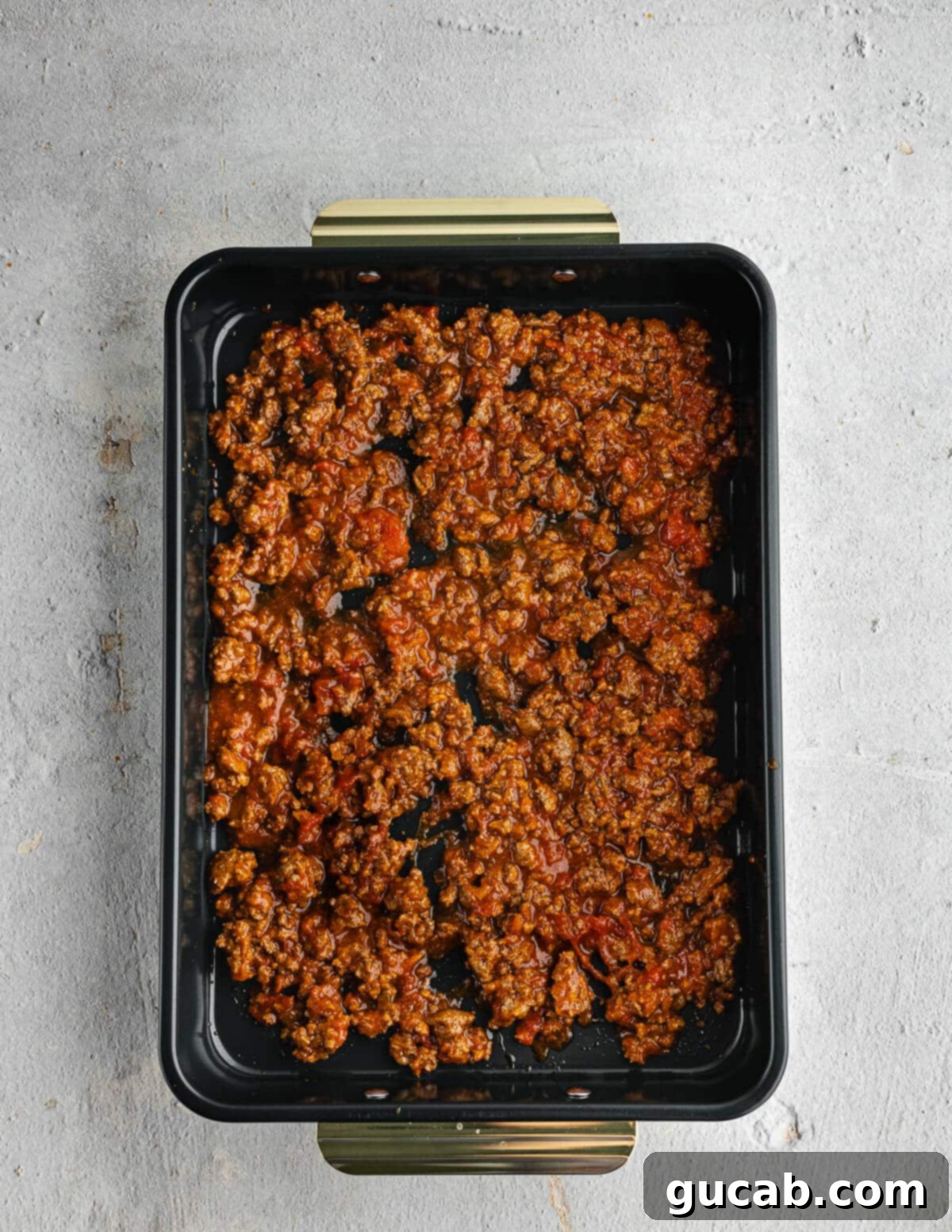 A baking dish with a layer of savory meat sauce spread evenly at the bottom.