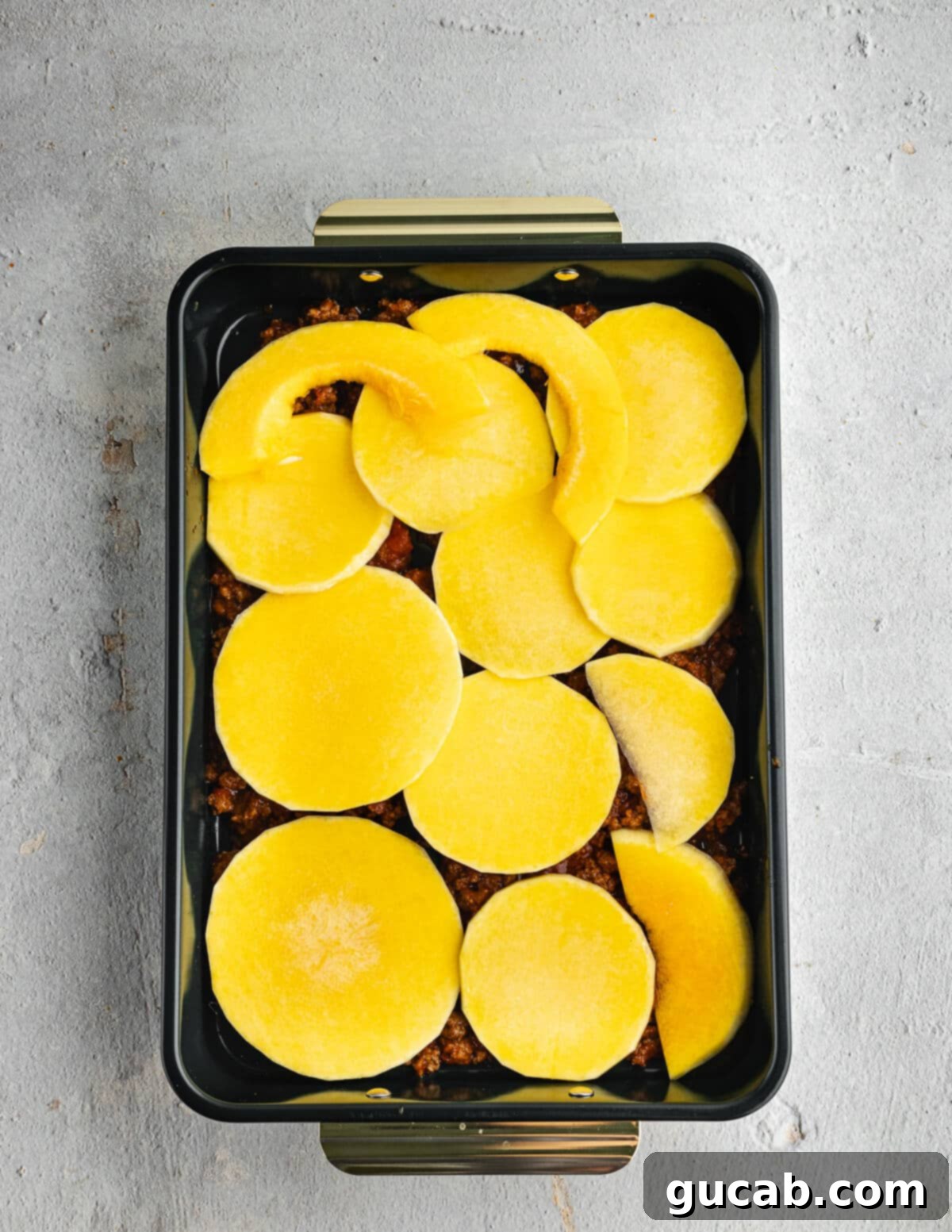 A baking dish showing the first layer of meat sauce topped with neatly arranged slices of butternut squash.