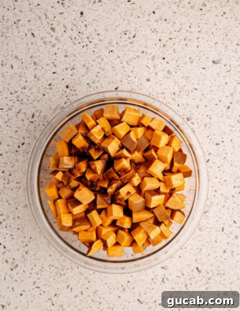 diced sweet potatoes in a bowl with cinnamon spiced coconut oil poured over it. 