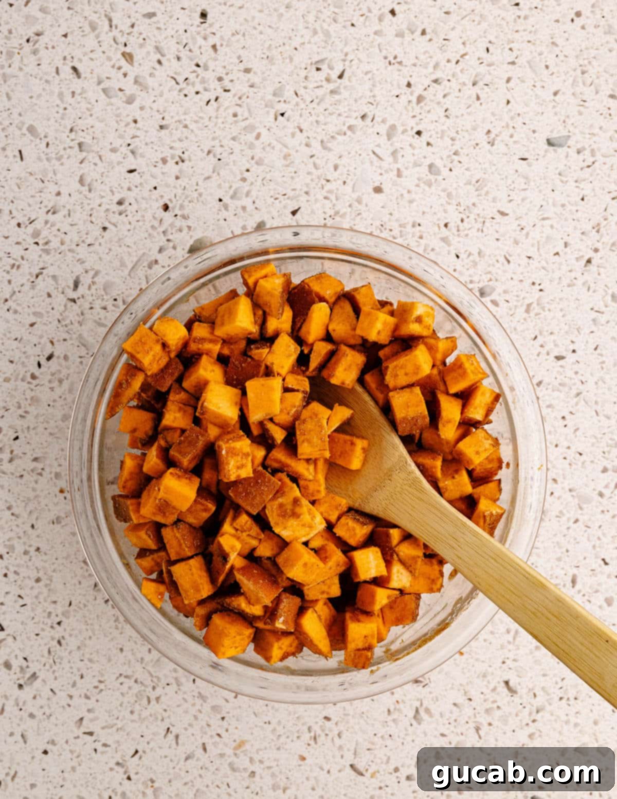 stirring diced sweet potatoes with cinnamon and coconut oil in a bowl. 
