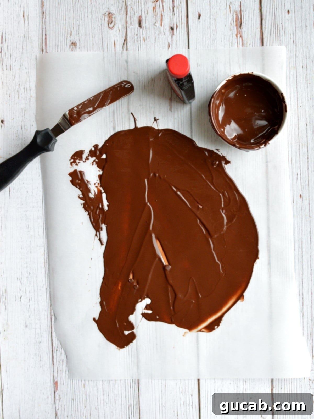 Melted chocolate spread thinly on parchment paper, ready to be chilled and flaked.