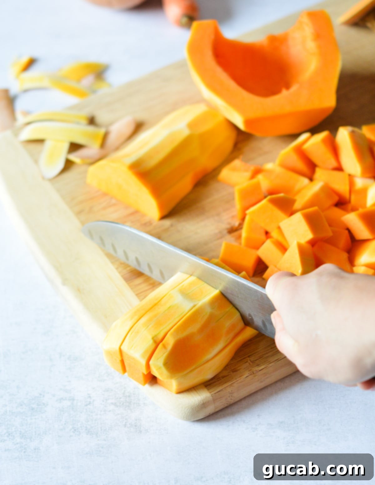 A knife actively dicing butternut squash strips into chunks, illustrating the preparation process.