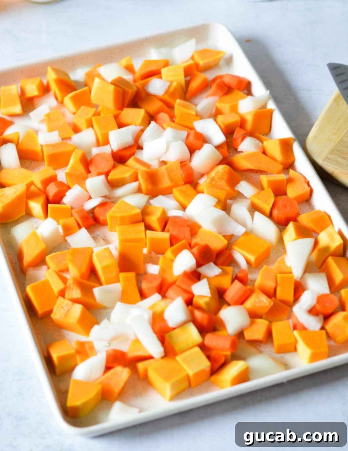 Butternut squash, onion, and carrots arranged on a sheet pan, ready for seasoning.
