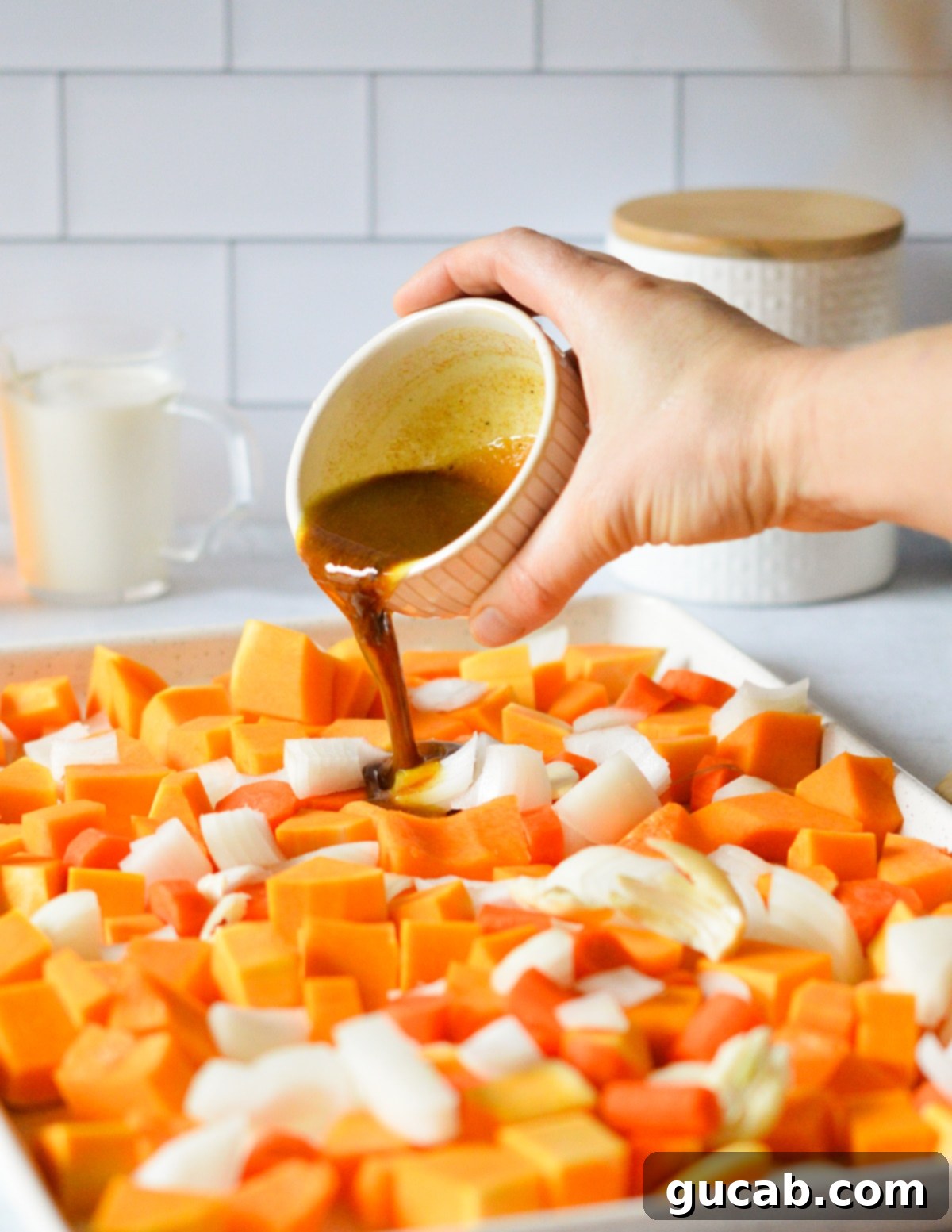 A hand pouring the butter and honey mixture over vegetables spread on a sheet pan.