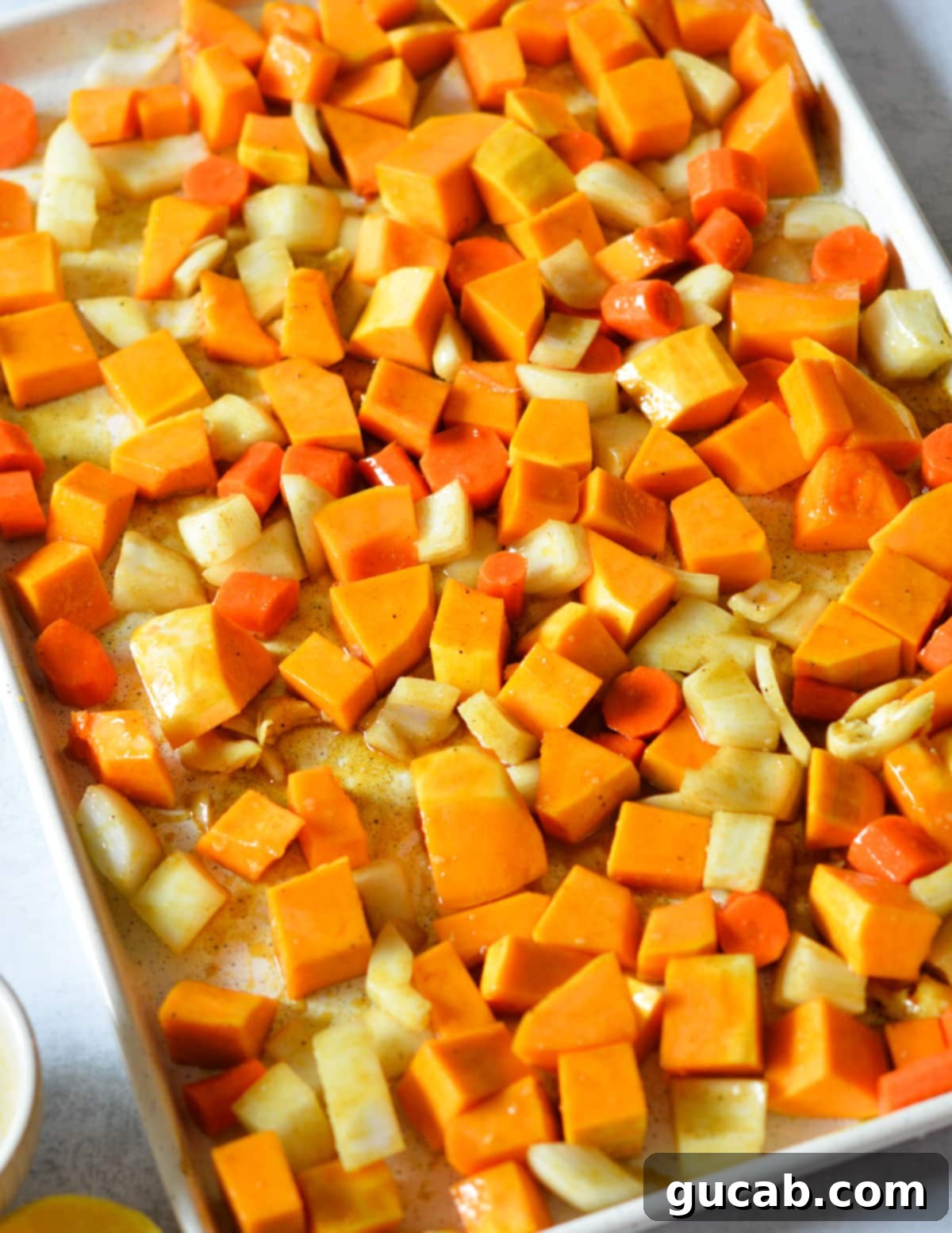 Roasted vegetables (butternut squash, onion, carrots) coated in butter, oil, and brown sugar on a sheet pan, ready for the oven.
