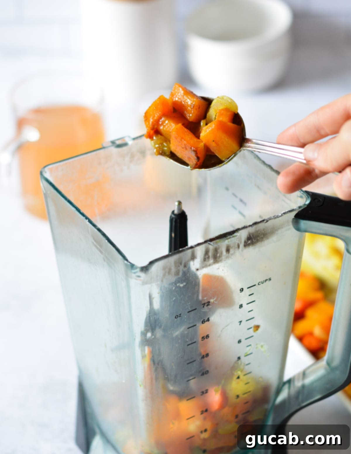 A hand scooping roasted squash into a high-speed blender.