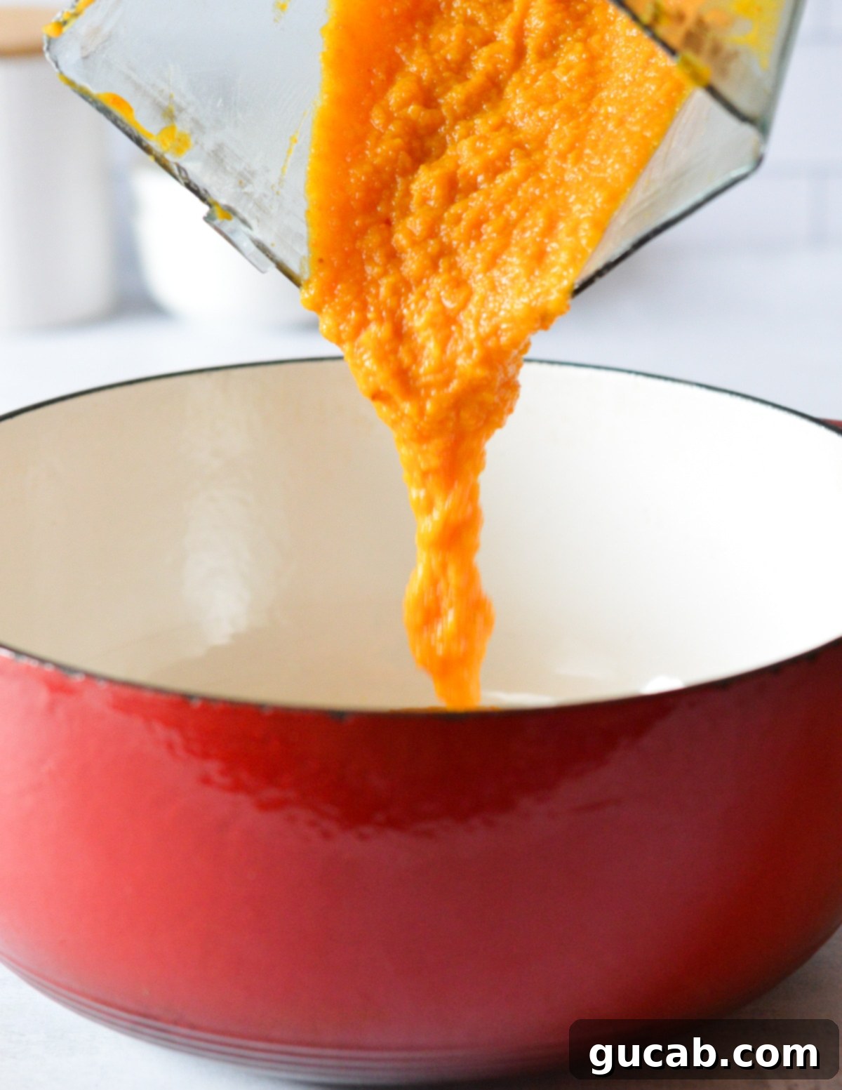A rich butternut squash puree being poured from a blender into a large dutch oven pot.