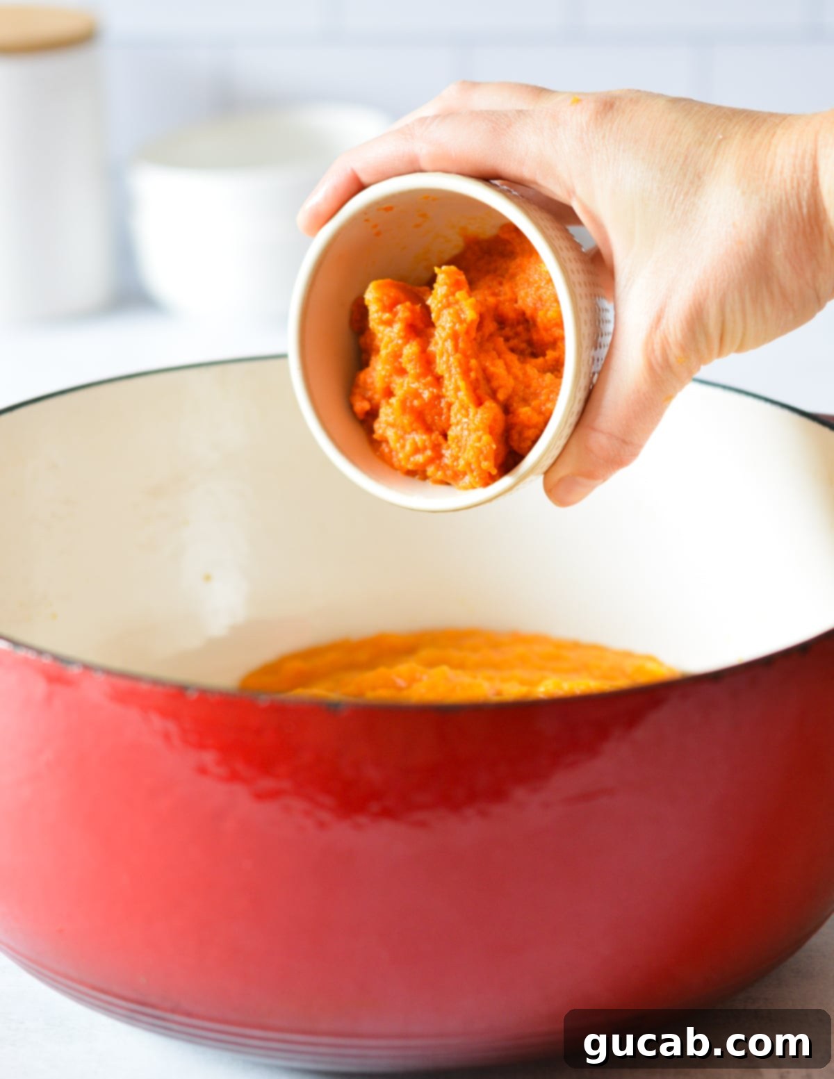 Pumpkin puree being added to a large pot filled with butternut squash puree.