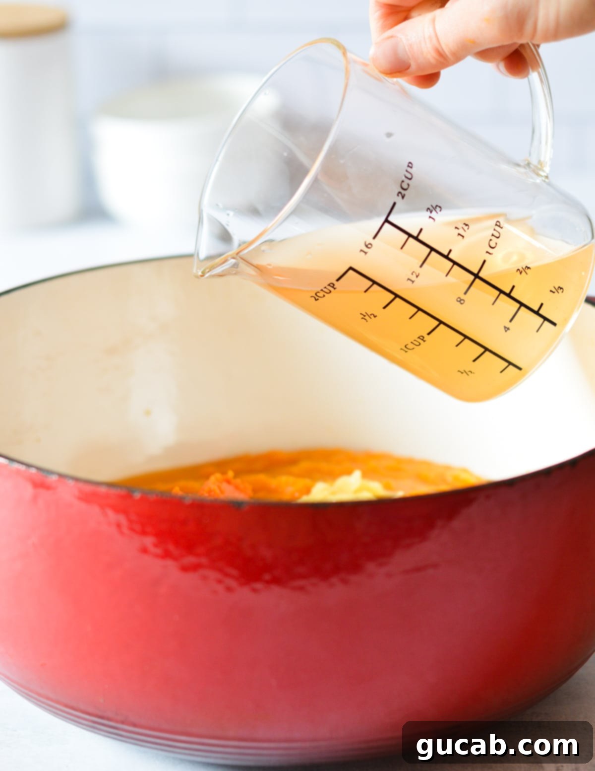 Vegetable stock being poured into a pot of butternut squash puree, ready for simmering.