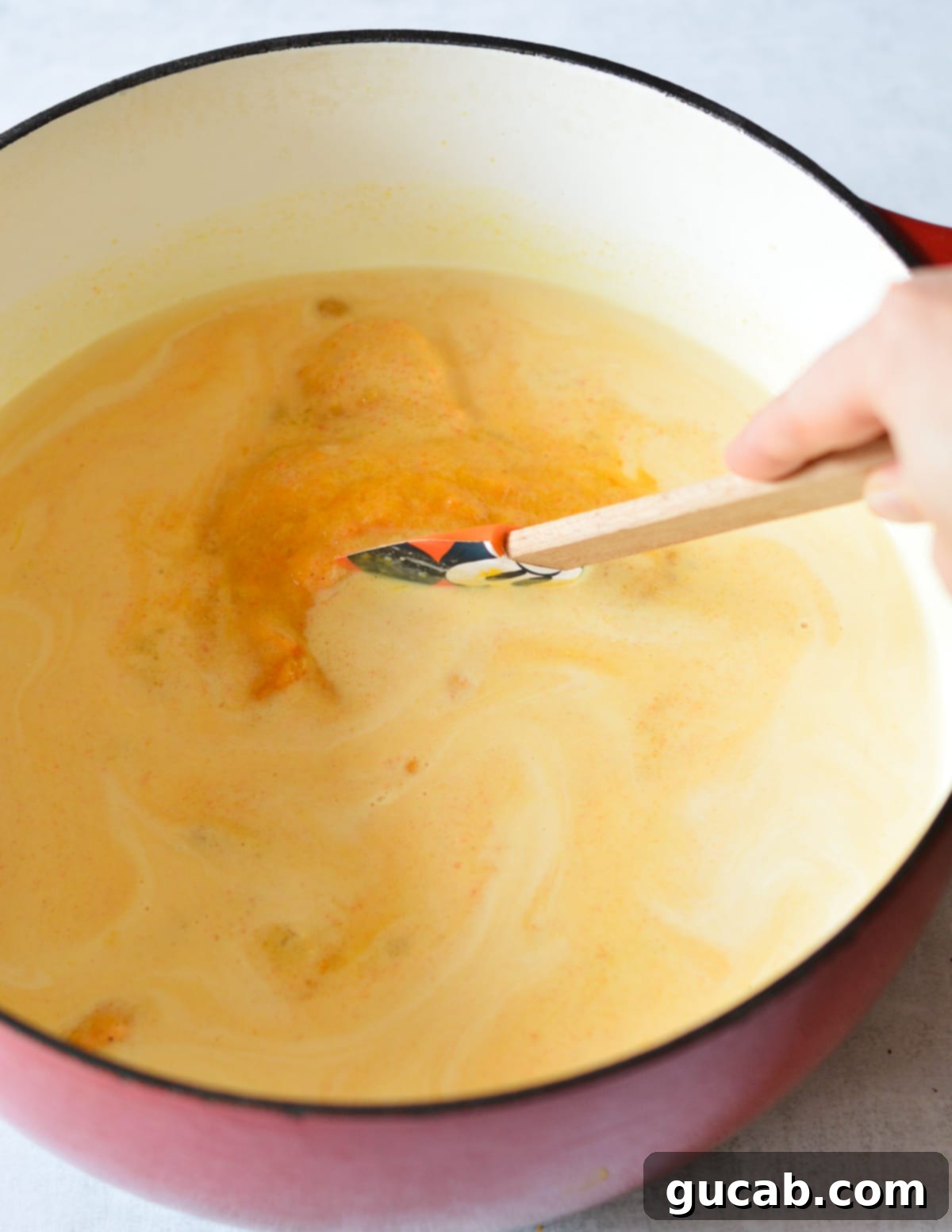 A spatula stirring heavy cream into butternut squash soup in a pot, creating a smooth blend.
