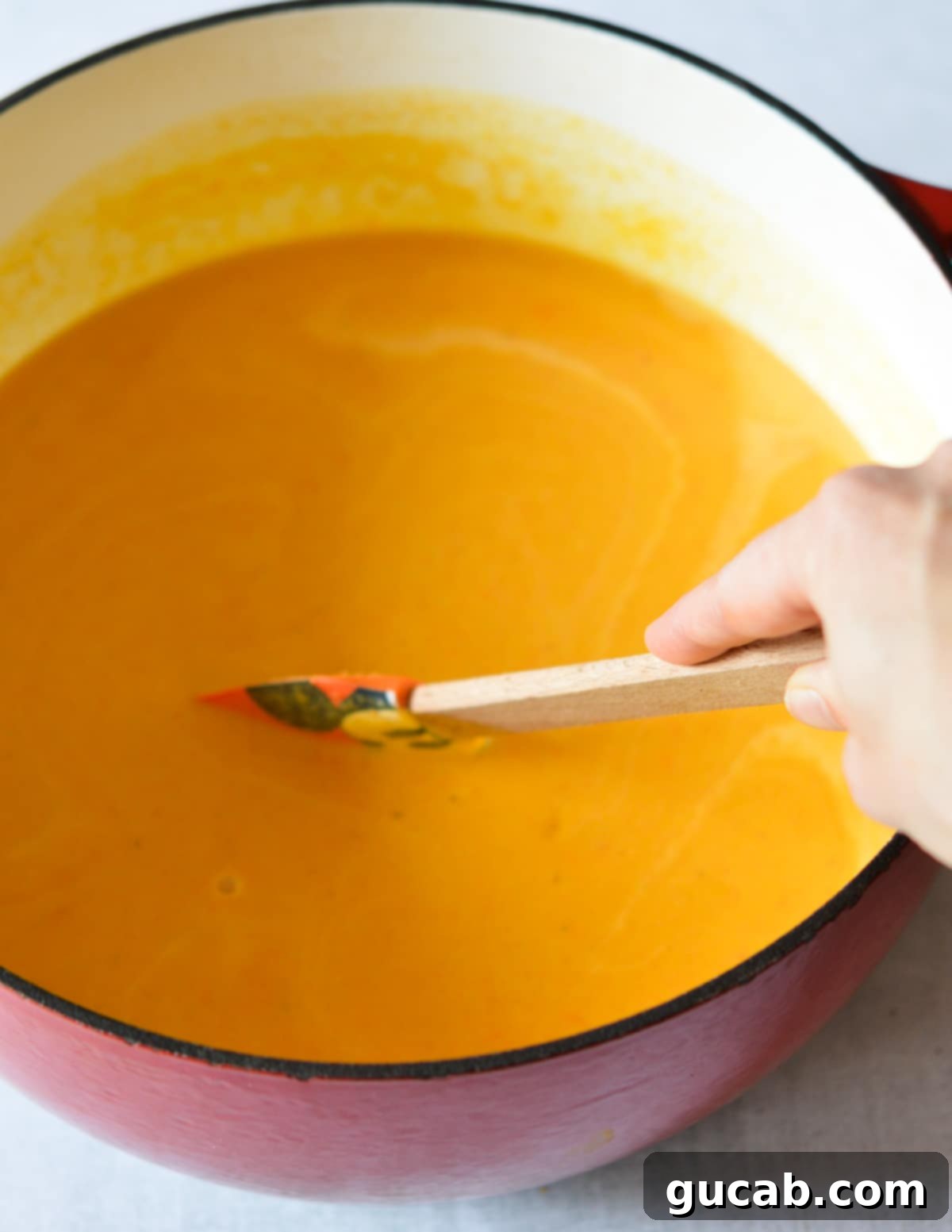 Butternut squash soup being stirred in a large orange dutch oven on the stovetop, ready to be served.