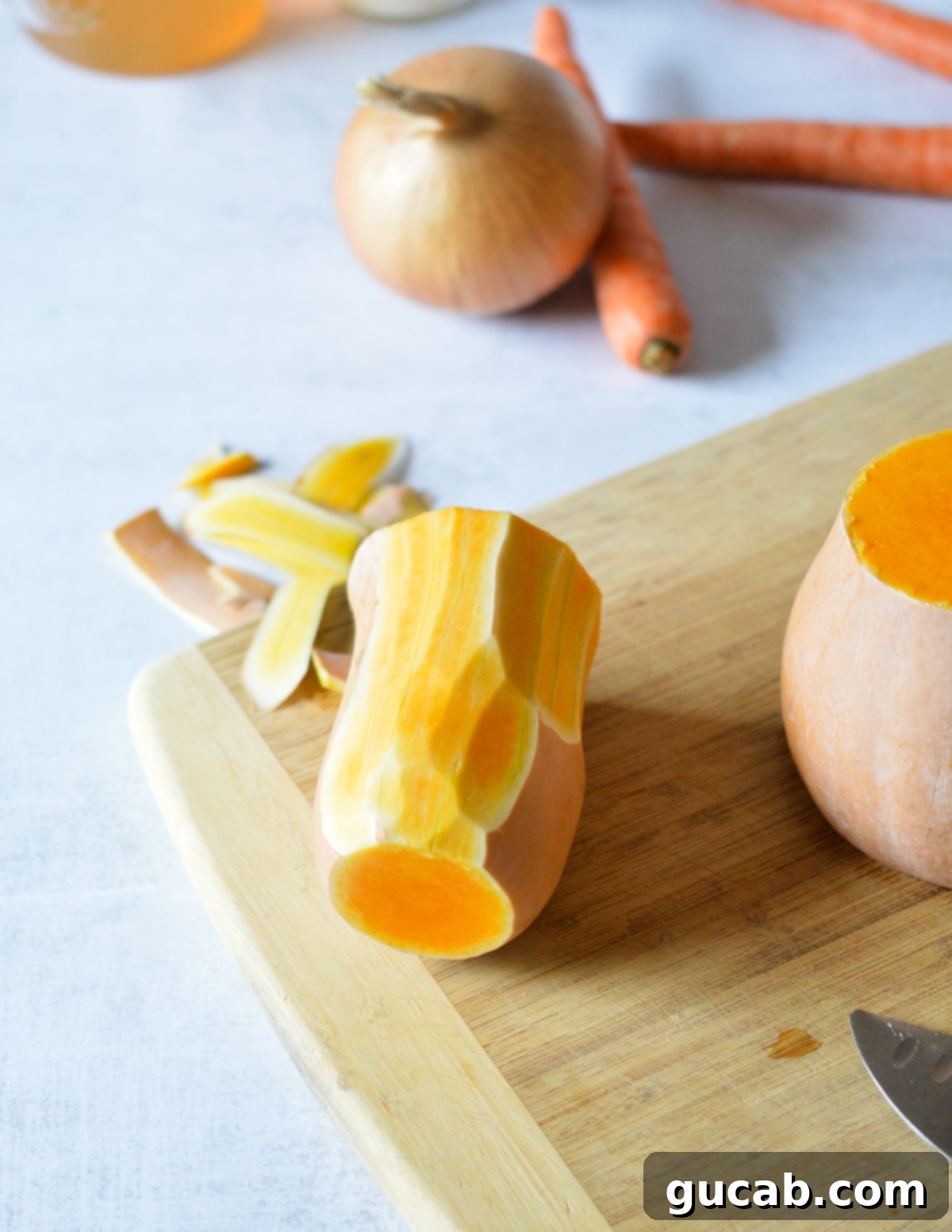 A peeled butternut squash neck resting on a cutting board, showcasing its smooth, orange flesh.