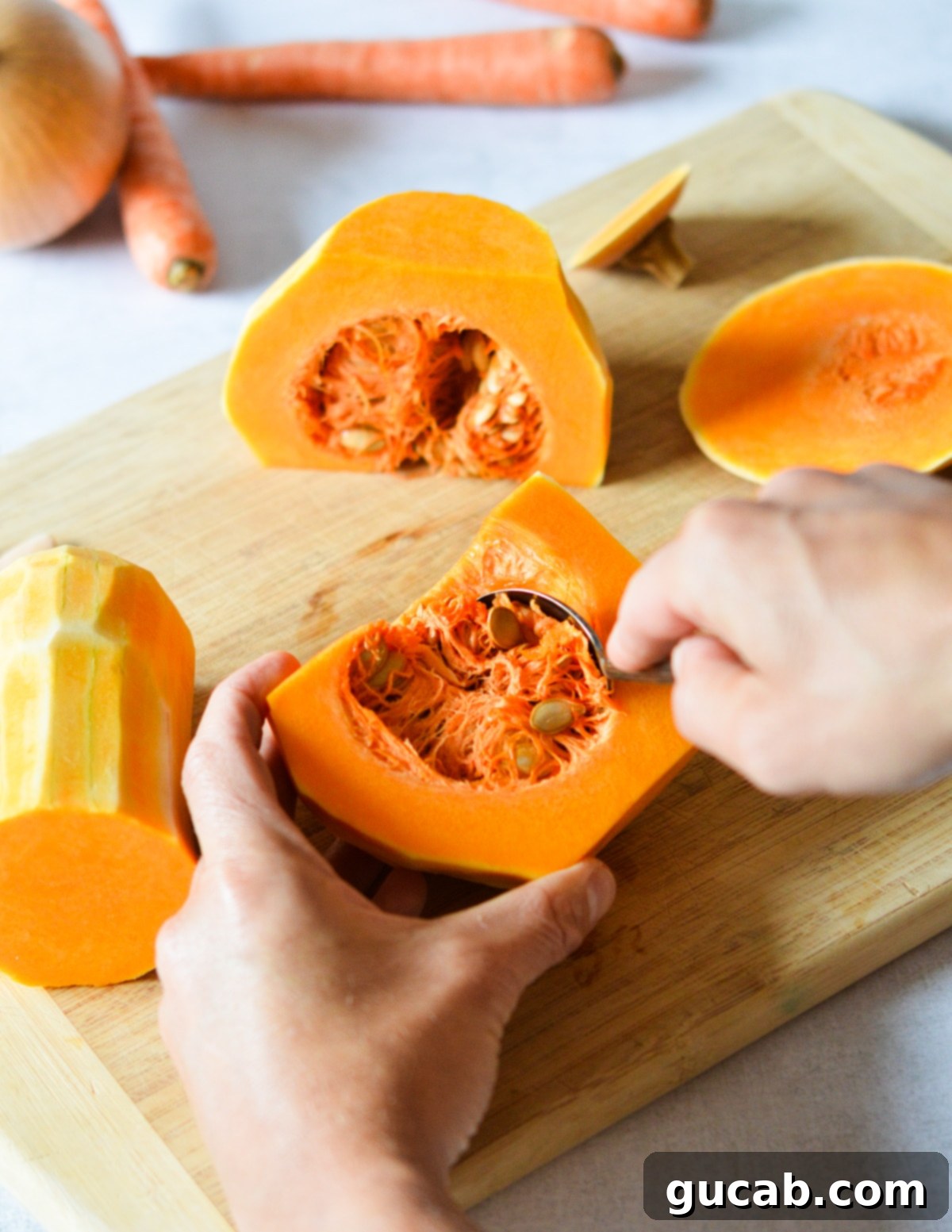 A hand using a large spoon to scoop out the seeds and fibrous goop from the inside of a halved butternut squash.