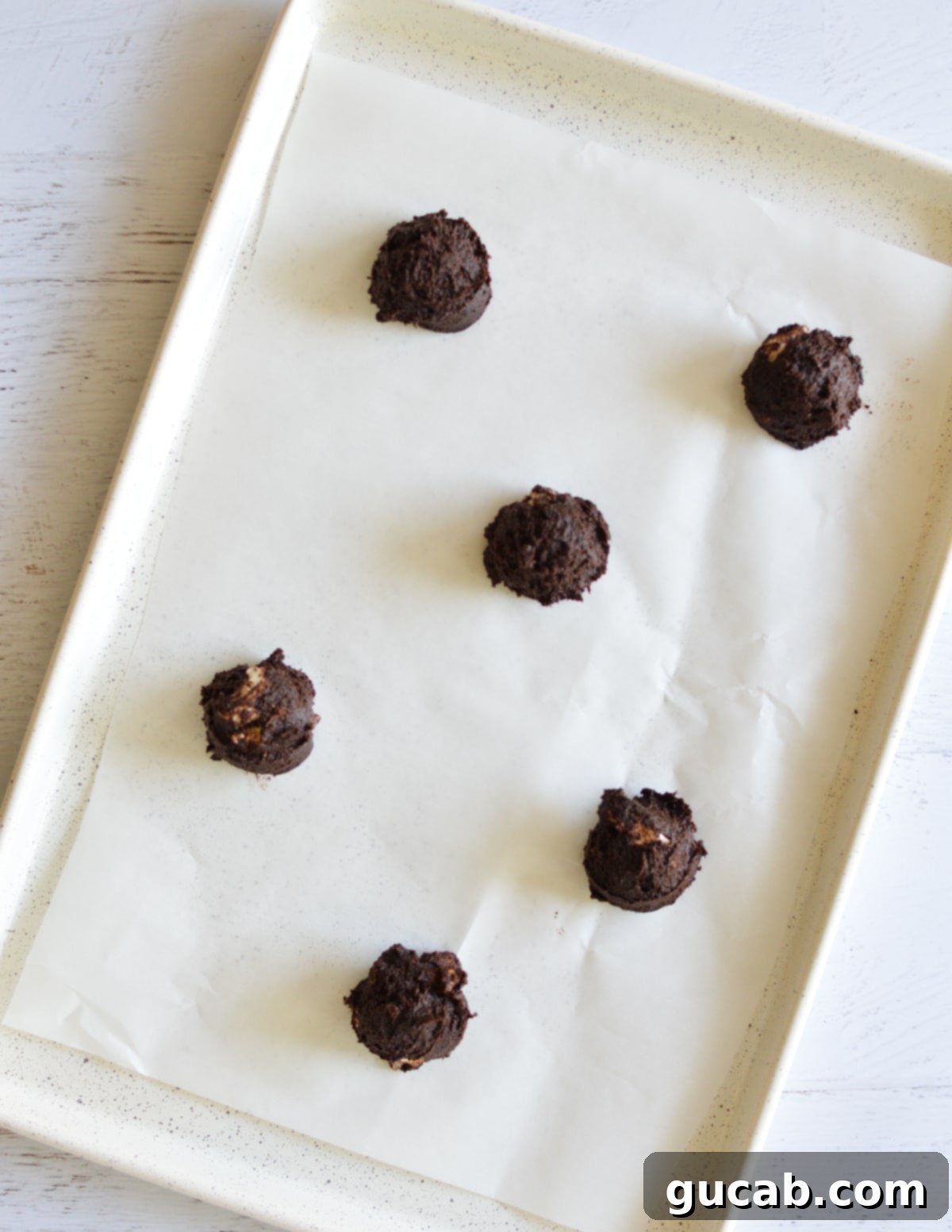 Unbaked chocolate marshmallow cookie dough balls, topped with mini marshmallows, arranged on a parchment-lined sheet pan.
