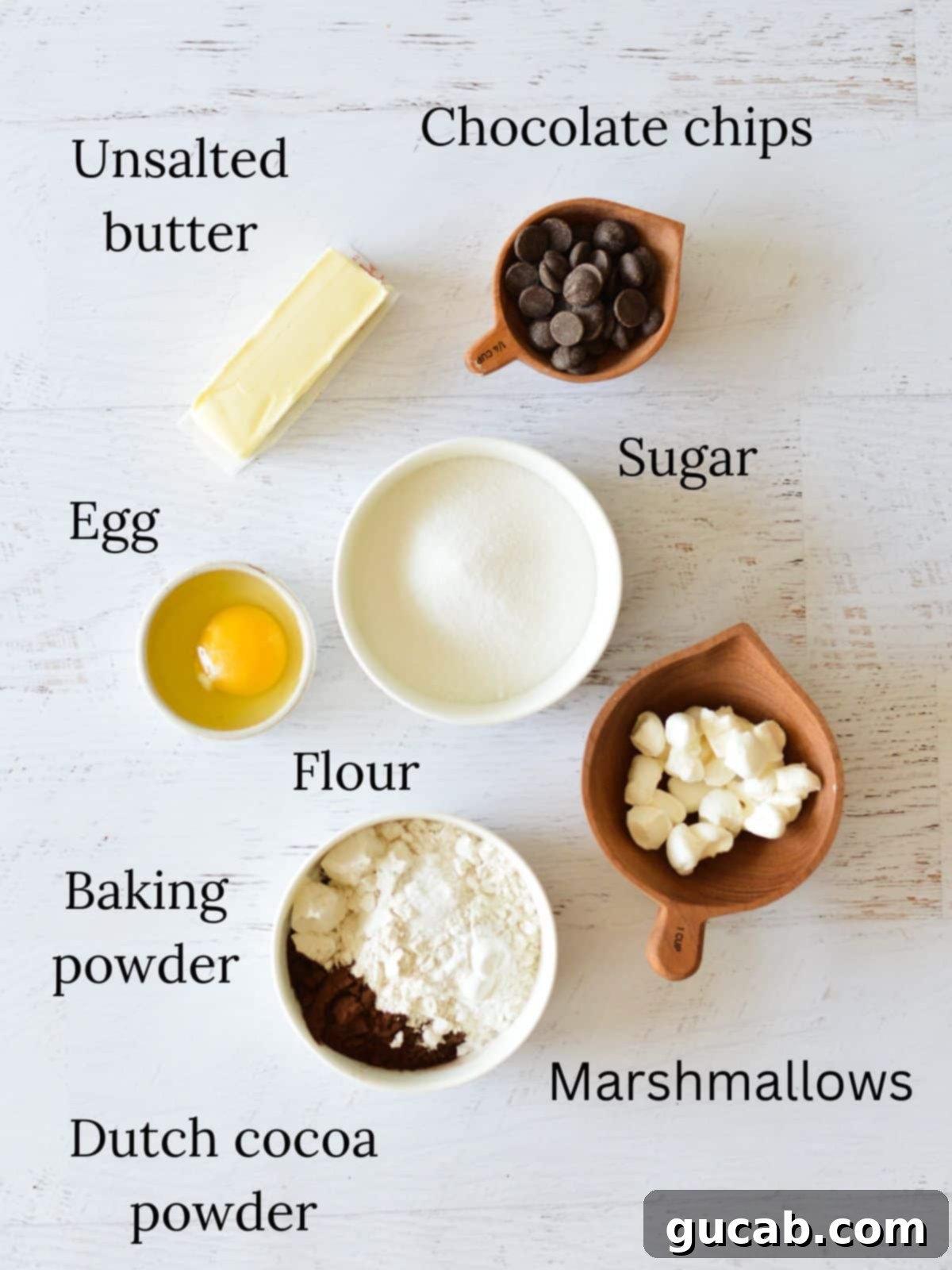 A collection of ingredients for baking chocolate marshmallow cookies, including butter, sugar, chocolate chips, cocoa powder, and marshmallows.