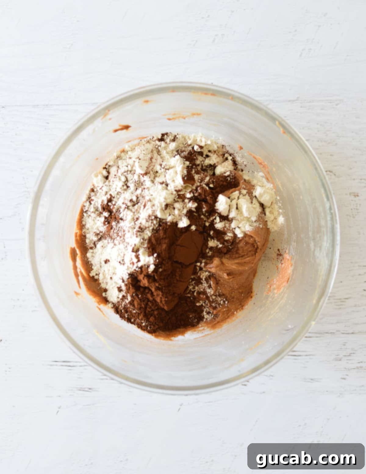 Dry ingredients including flour and dark cocoa powder added to the wet mixture in a bowl.