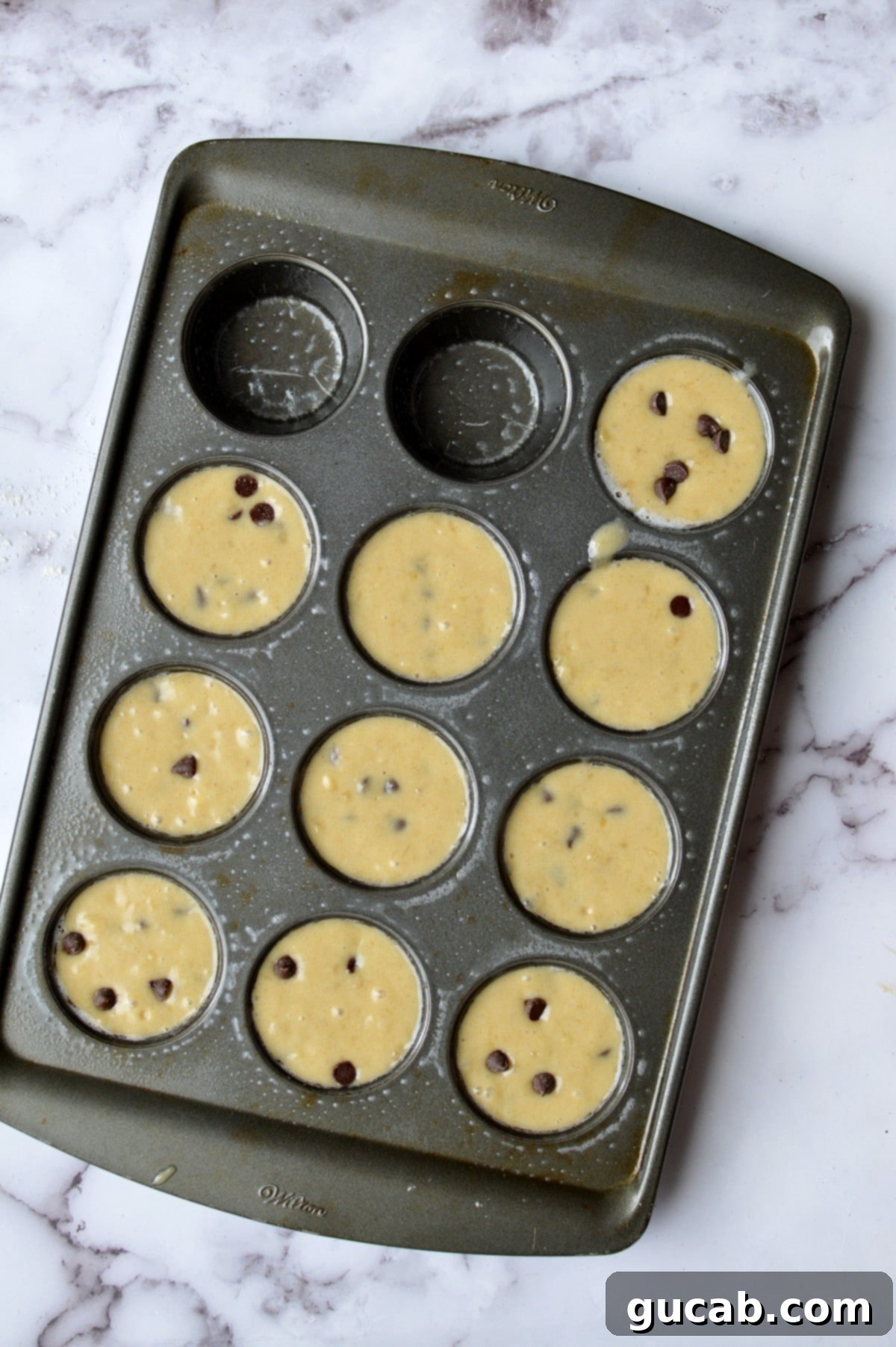 A muffin tin filled with gluten-free banana chocolate chip muffin batter, ready for baking