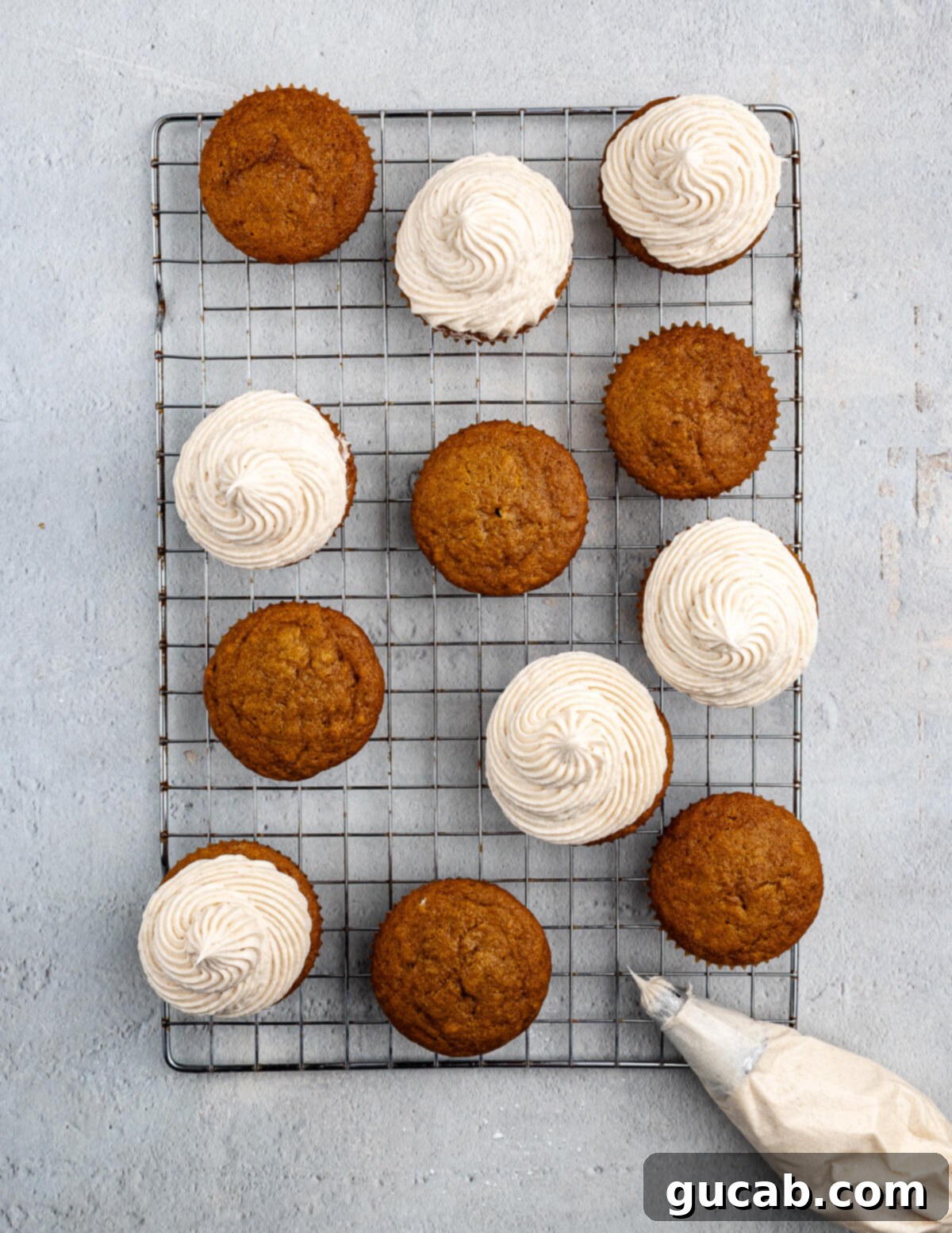 Golden Pumpkin Bliss: Gluten-Free Maple-Cinnamon Cupcakes 15 Pumpkin cupcakes cooling on a wire rack, with some already frosted and others waiting, showcasing the baking process.