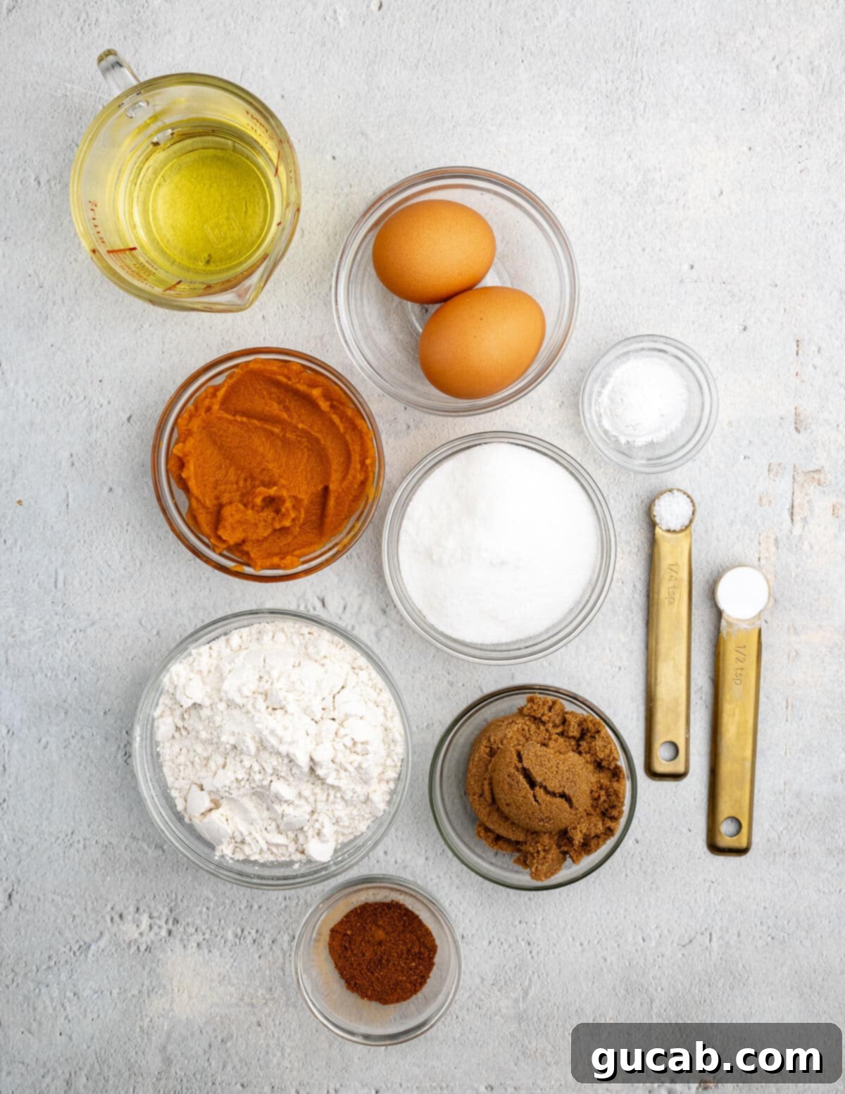 Spiced Gluten Free Pumpkin Cupcakes with Cinnamon Maple Frosting 3 A collection of key ingredients for gluten-free pumpkin cupcakes, including vegetable oil, eggs, pumpkin puree, baking powder, sugars, gluten-free flour, and pumpkin pie spice, laid out on a kitchen counter.