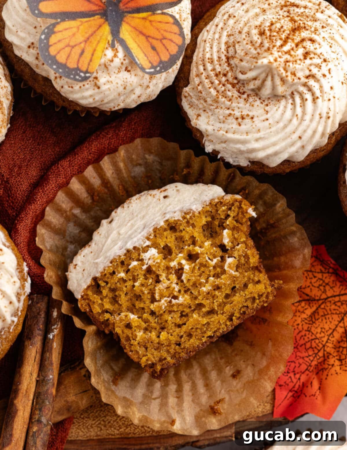 Spiced Gluten Free Pumpkin Cupcakes with Cinnamon Maple Frosting 4 A perfectly baked gluten-free pumpkin cupcake, cut in half to show its moist texture, still in its paper liner, with a dollop of maple frosting.