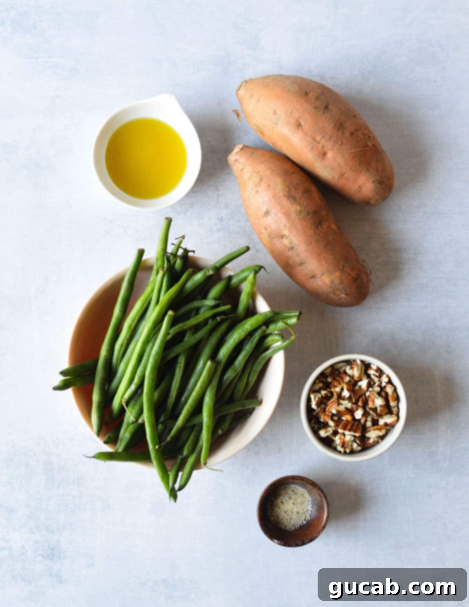 Perfectly Roasted Green Beans and Sweet Potatoes 3 Close-up of fresh sweet potatoes, green beans, olive oil, pecans, and various spices laid out on a table, ready for roasting.