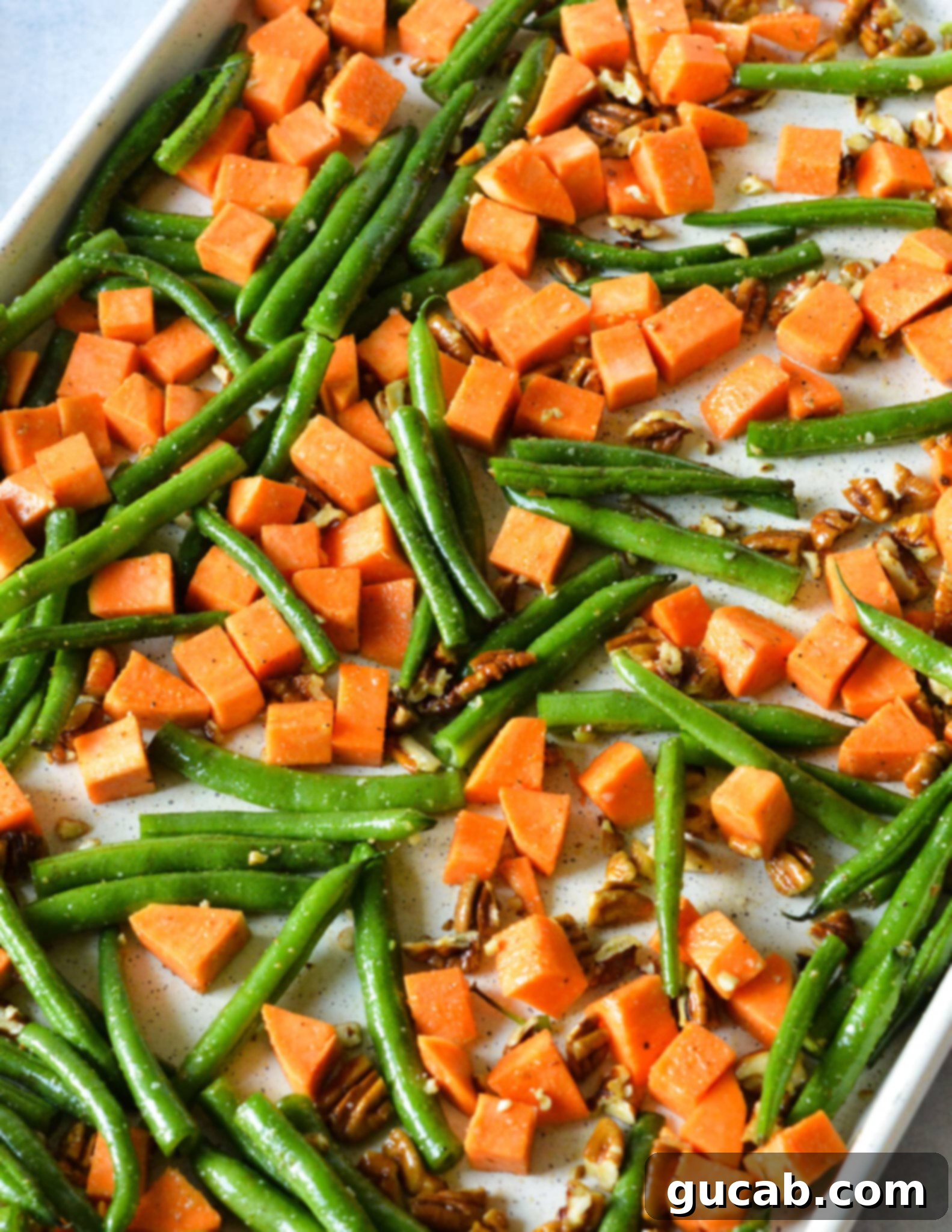 Perfectly Roasted Green Beans and Sweet Potatoes 8 Raw sweet potatoes, green beans, and pecans evenly spread on a sheet pan, coated in oil and spices, ready for the oven.